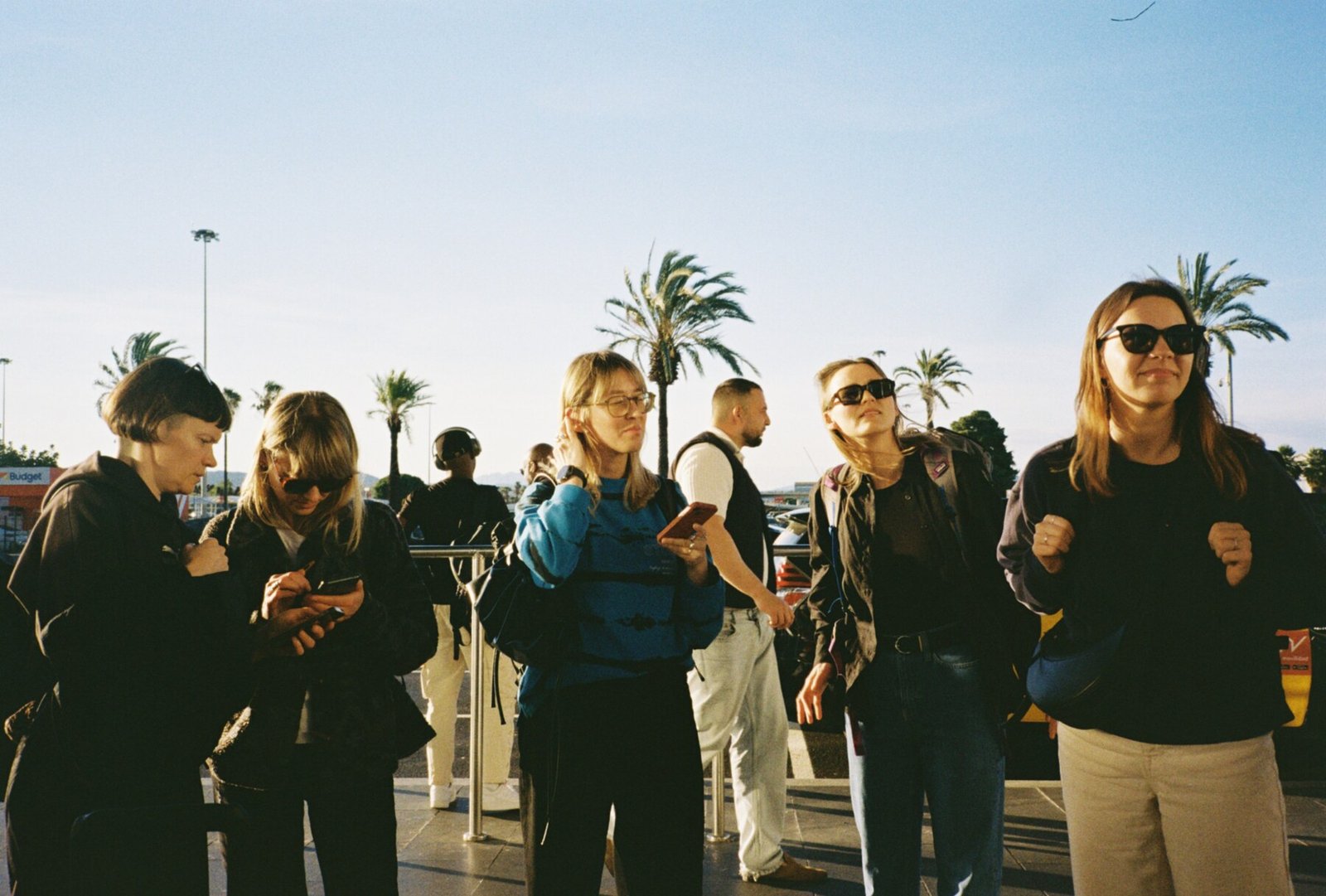 Andstudio team members stand together outdoors in front of palm trees on a sunny day, wearing casual black clothing and sunglasses
