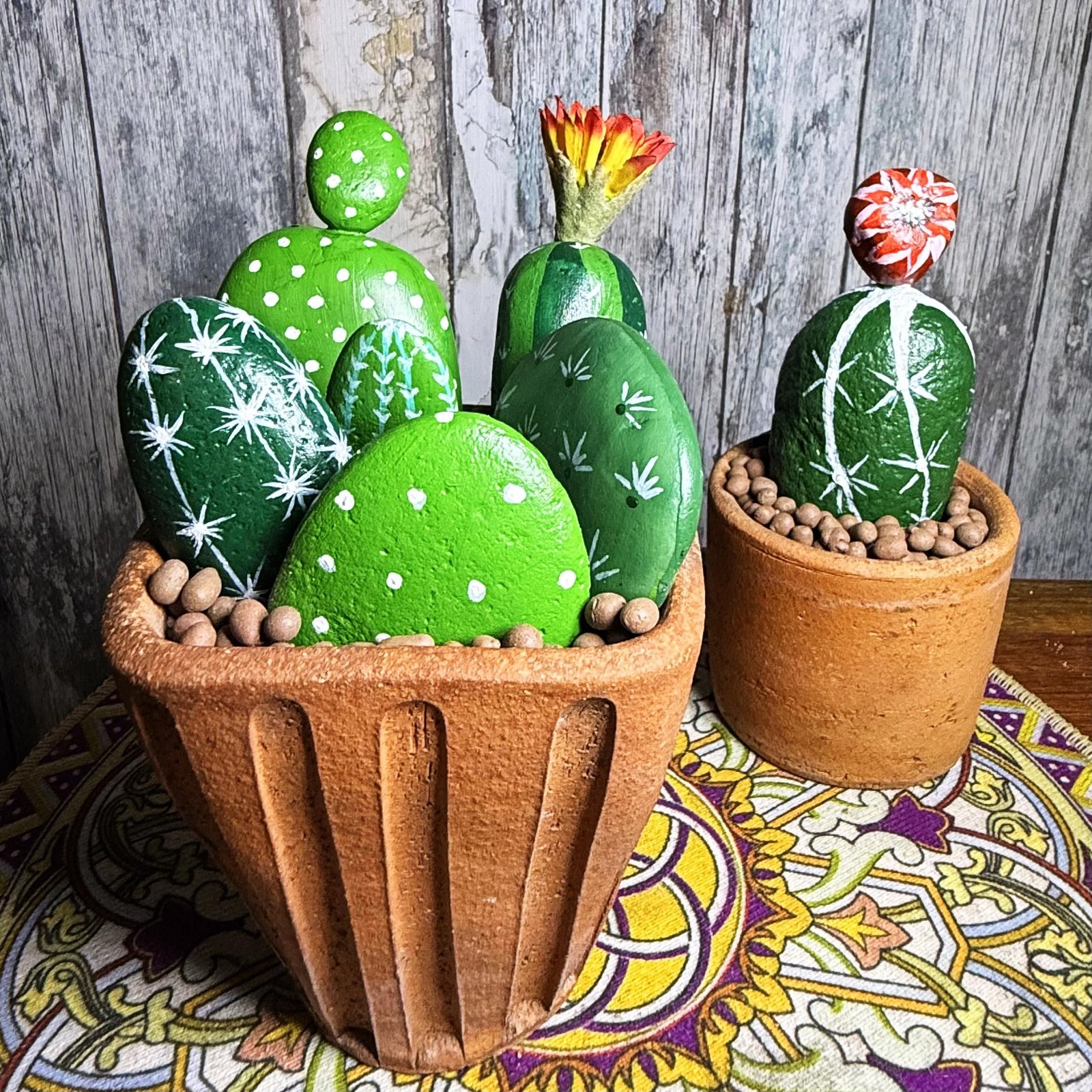 Two terracotta pots filled with finished hand-painted stone cactus plants against a wooden backdrop