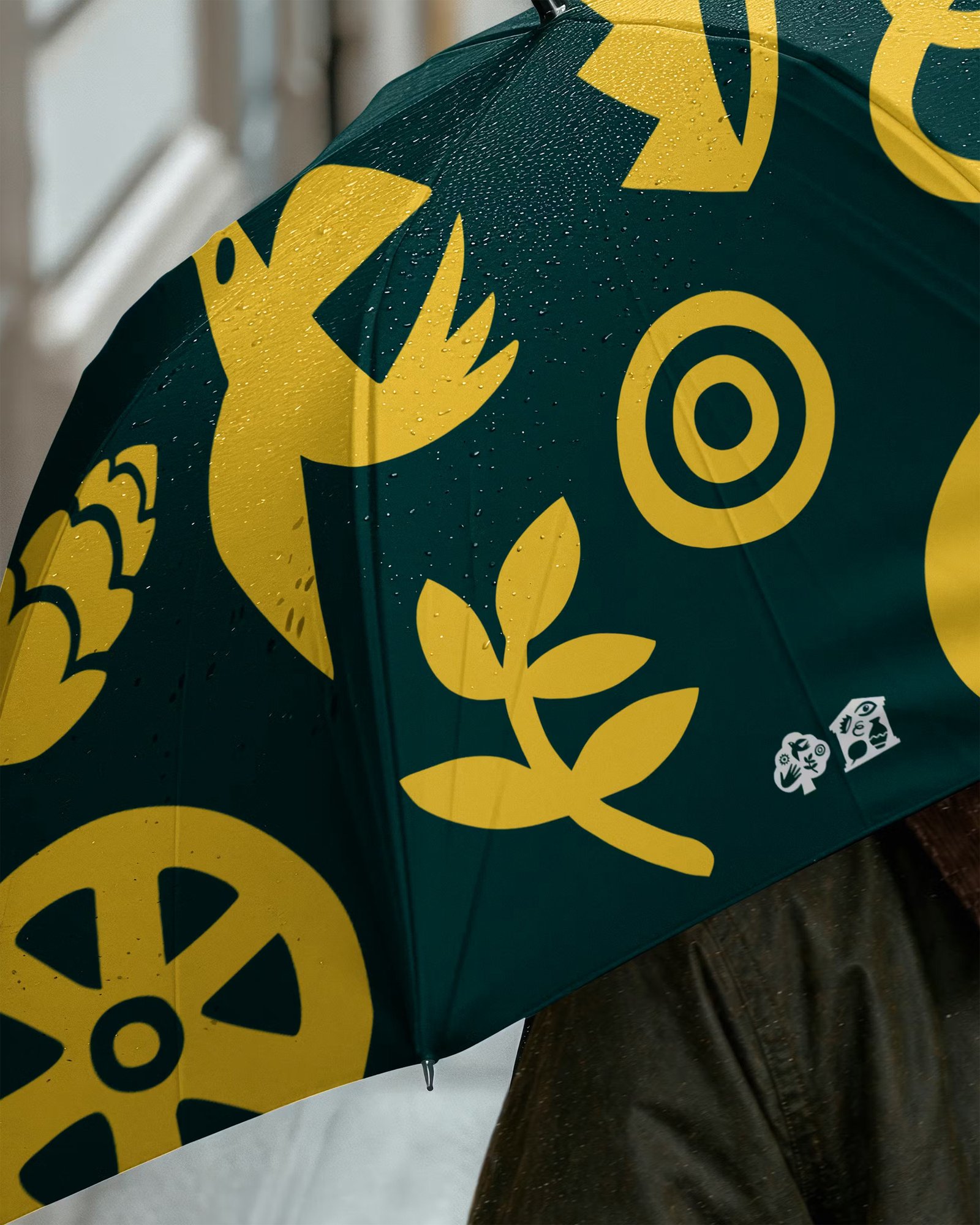 Dark teal umbrella with bold yellow botanical and geometric motifs including leaves, flowers and circular patterns, featuring the Gunnersbury rebrand identity