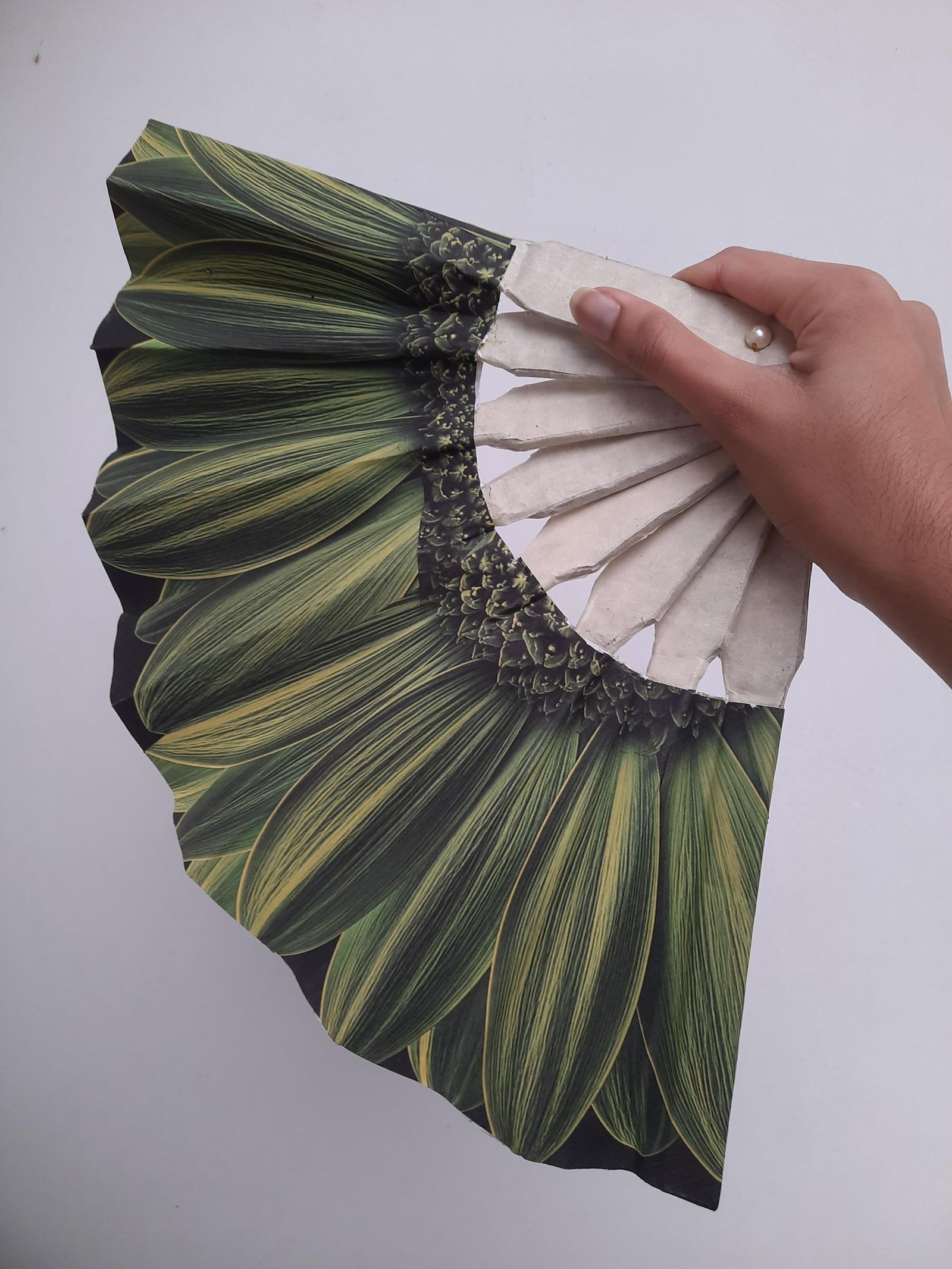 An open handmade botanical fan held by its cardboard handle
