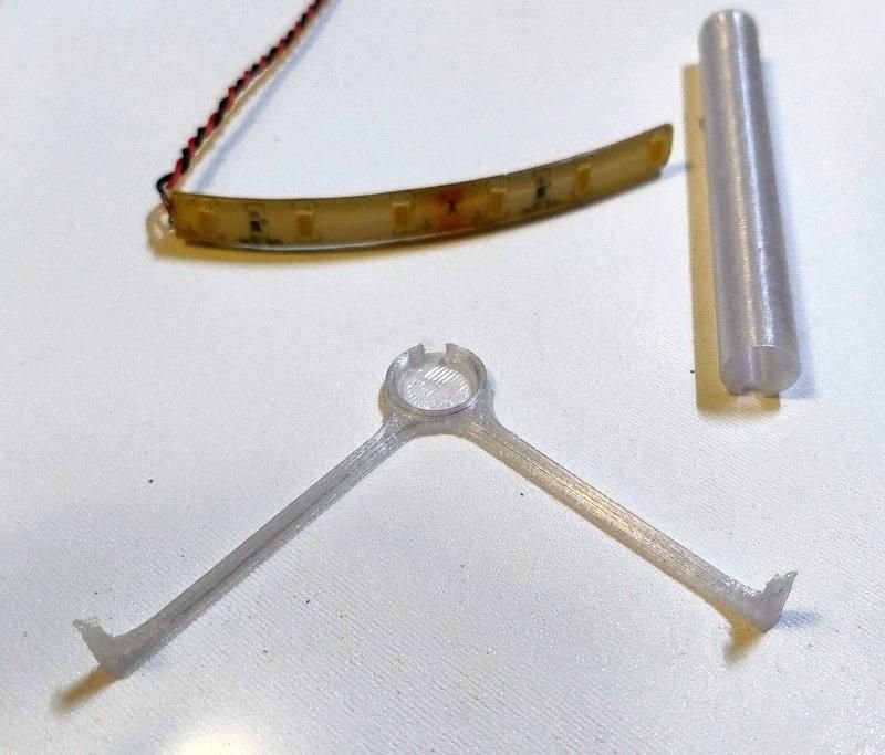 LED strip, translucent cylindrical diffuser, and transparent 3D-printed tripod holder arranged on a white surface