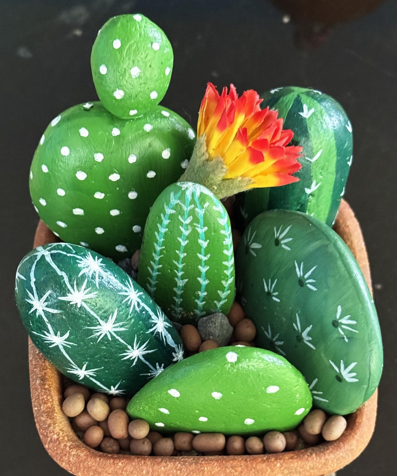 Close-up of a finished terracotta planter filled with green stone cactuses and a bright flower