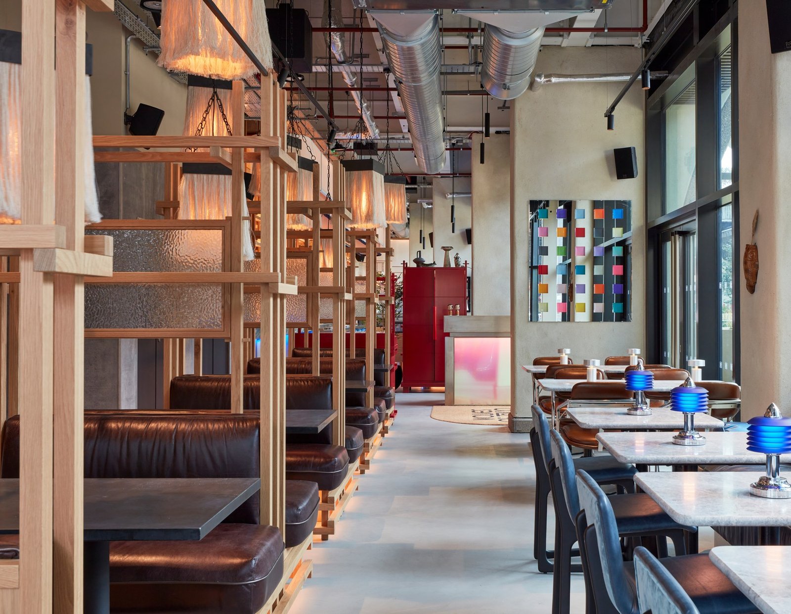 Interior of Wolves of Tokyo restaurant showing wooden booth seating on the left, dining tables with blue glassware on the right, and colourful artwork on the walls