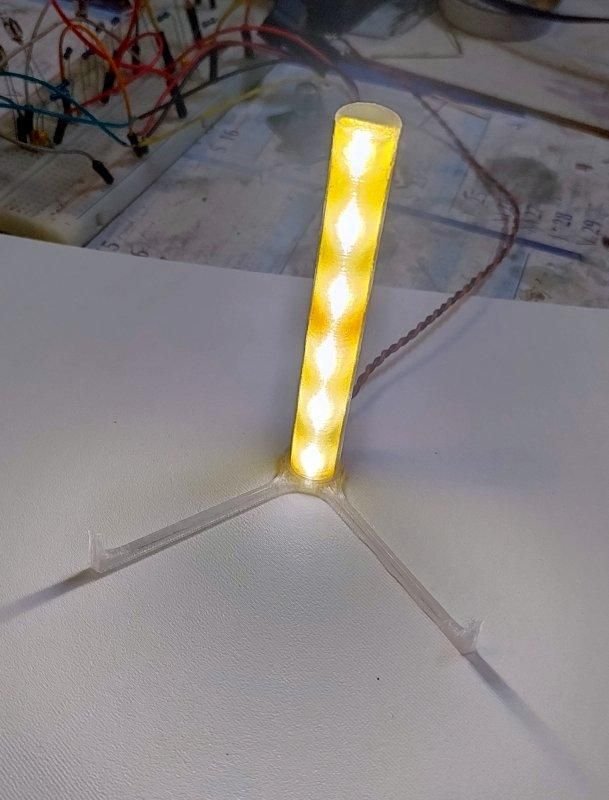 Glowing cylindrical LED diffuser mounted vertically in a clear three-legged holder during a bench test