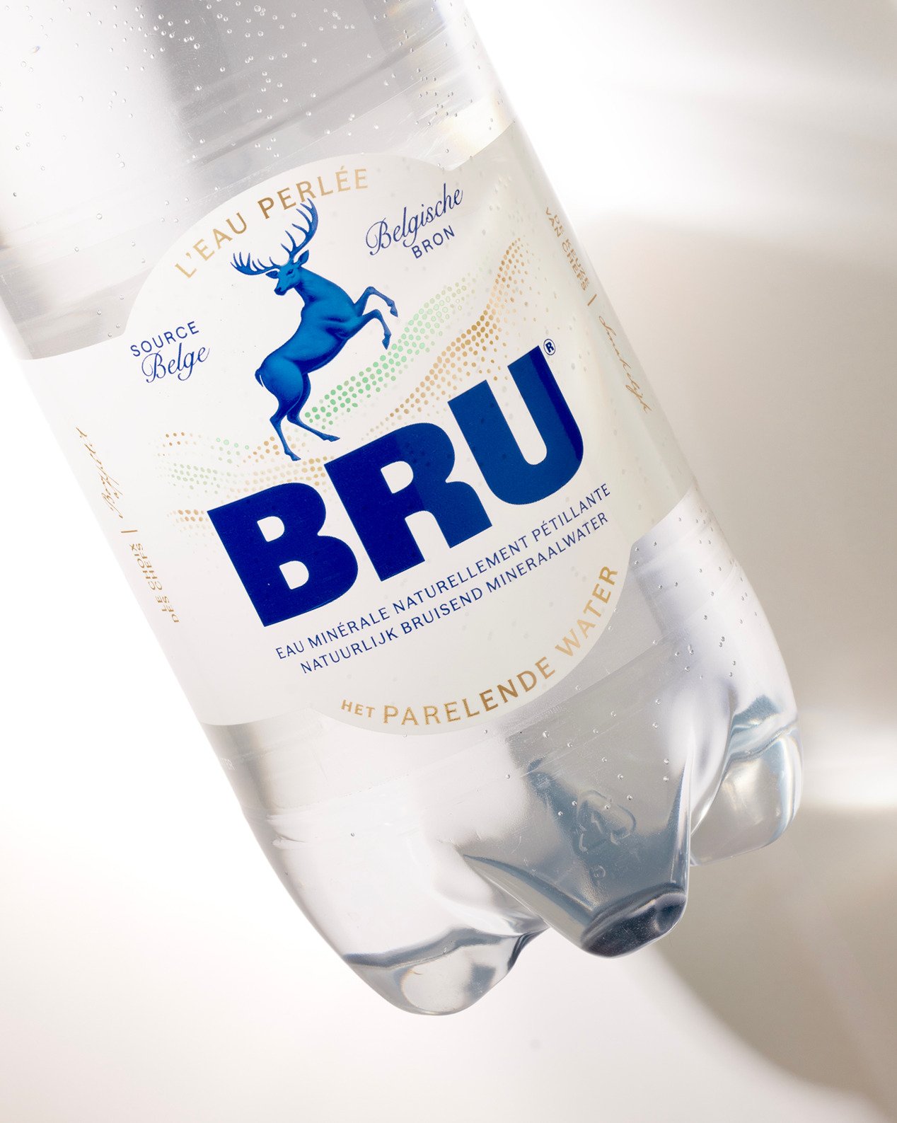 Bottle of BRU sparkling water with a redesigned label featuring a blue leaping stag and bold typography against a white background