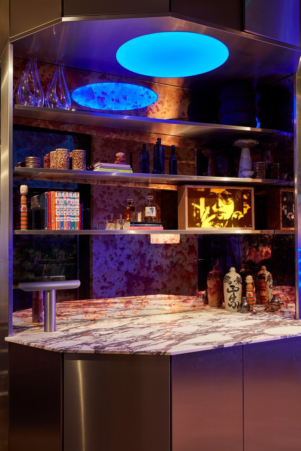 Illuminated display shelving at Wolves of Tokyo with blue-glowing ceiling panels, lacquer red accents, and carefully curated objects arranged against textured purple-toned walls