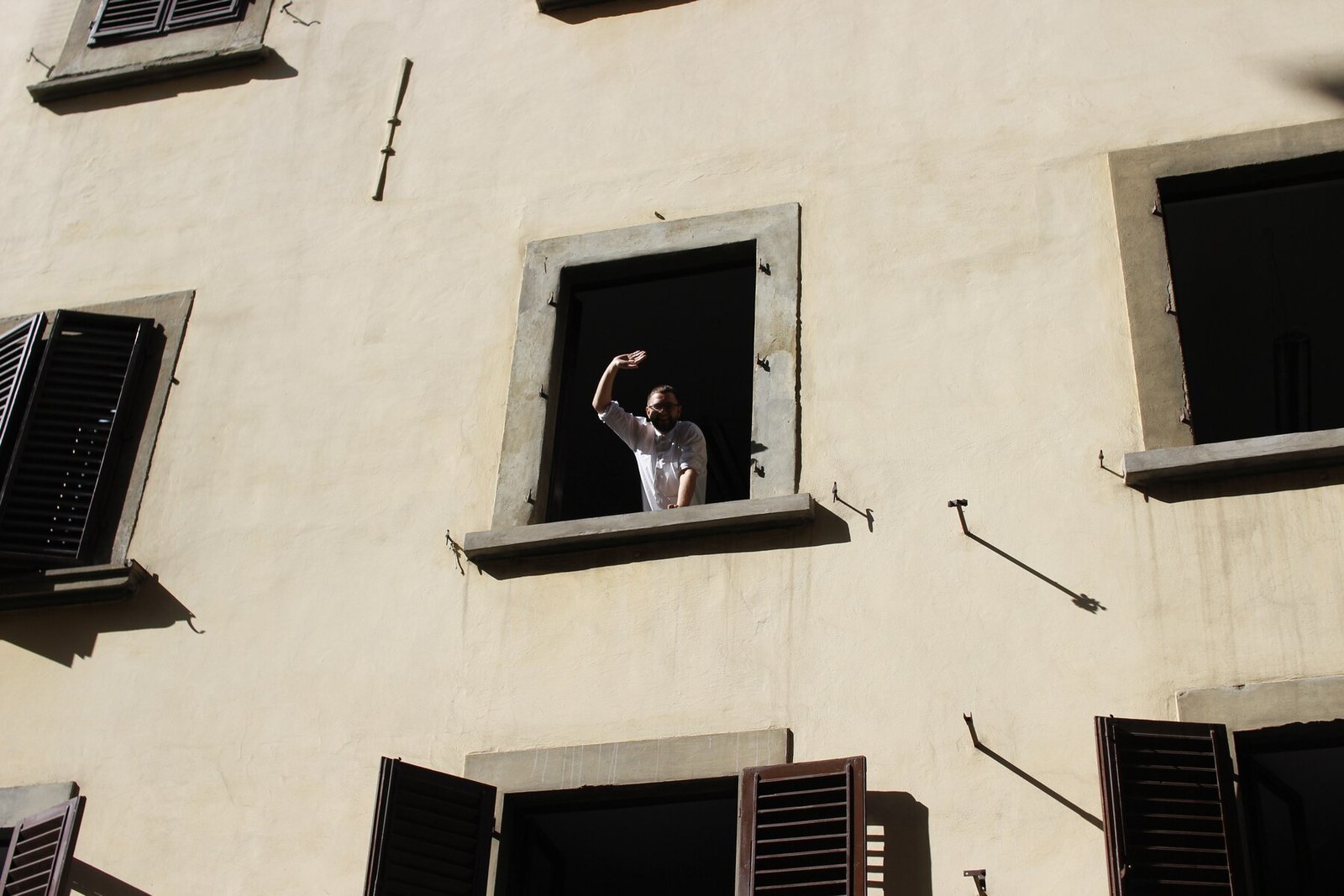 Person leaning out of a window on a cream-coloured building facade with scattered windows and shutters