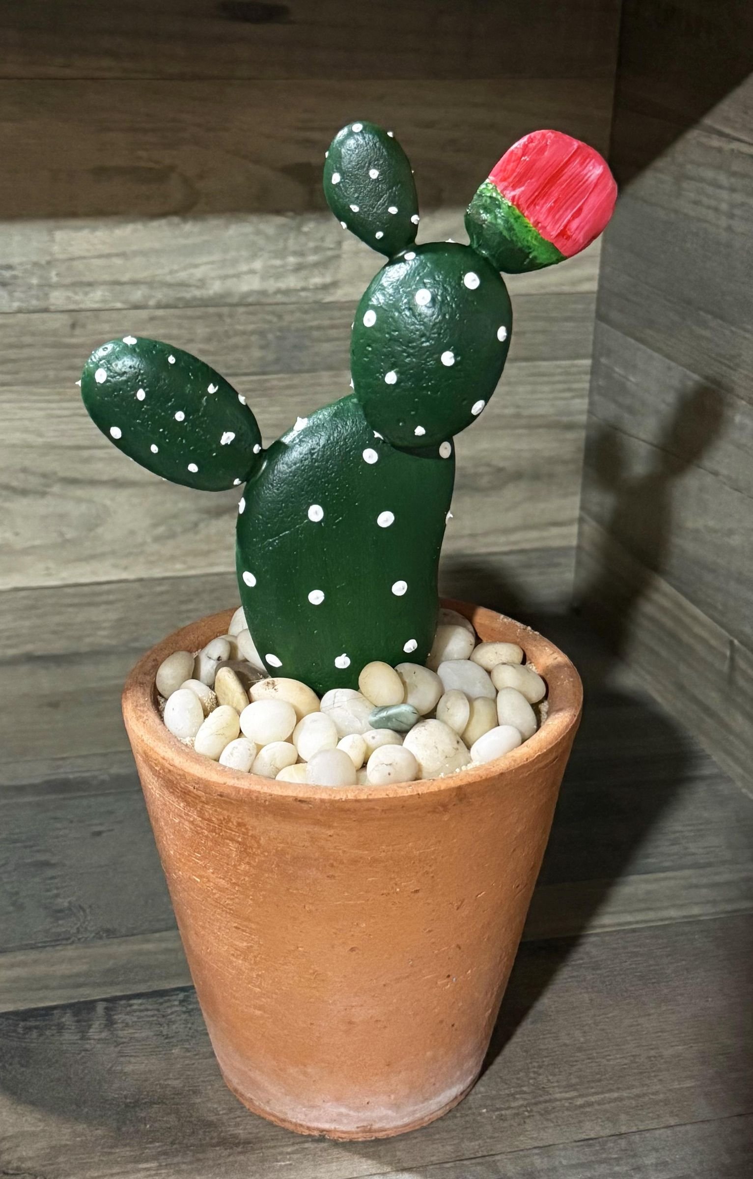 A finished prickly pear-shaped stone cactus with a red flower in a small terracotta pot