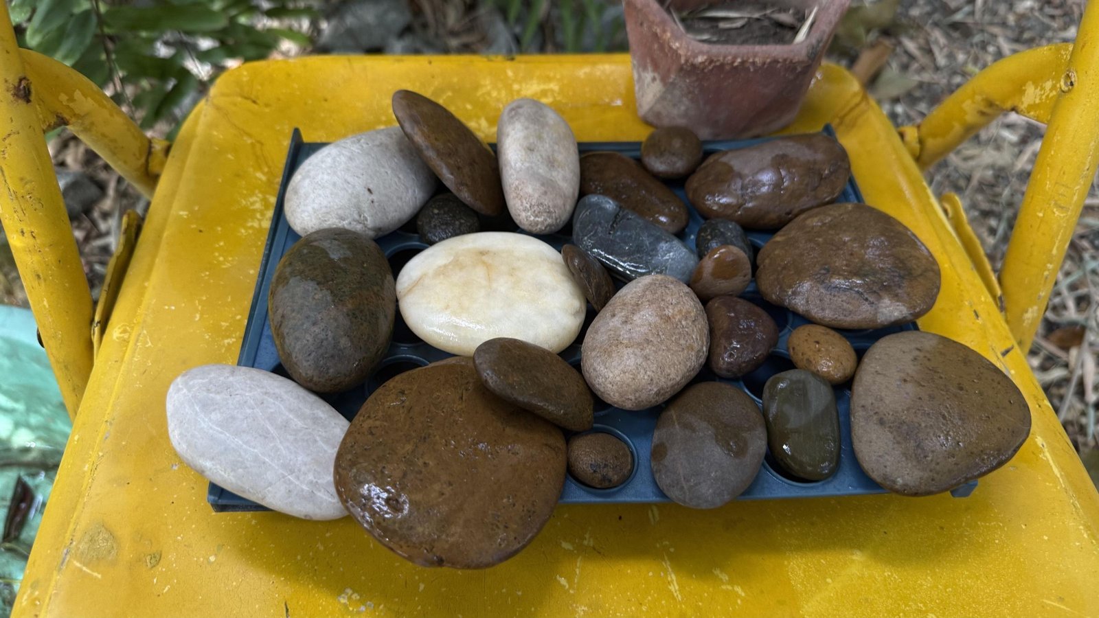Assorted smooth river-style stones in different sizes and shapes on a yellow tray