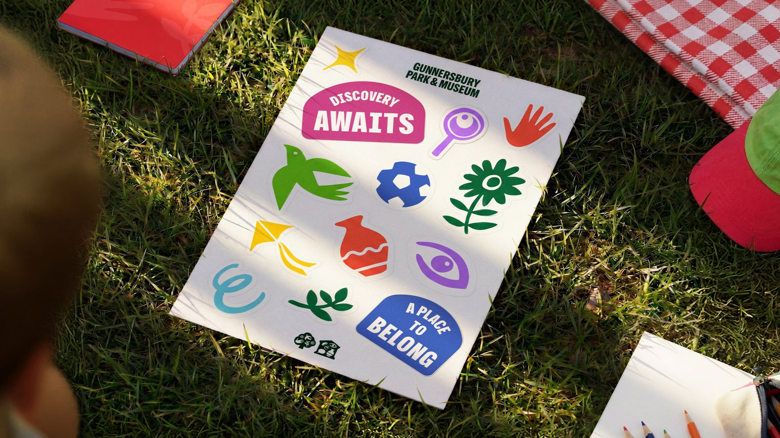 Rebrand identity sheet on grass featuring ‘Discovery Awaits’ and ‘A Place to Belong’ messages with colourful icons including plants, tools and abstract shapes