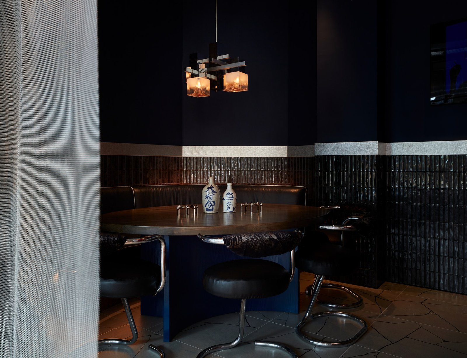 Dimly lit dining area at Wolves of Tokyo with a wooden table set with blue chairs, pendant lights overhead, and dark wood panelling on the walls
