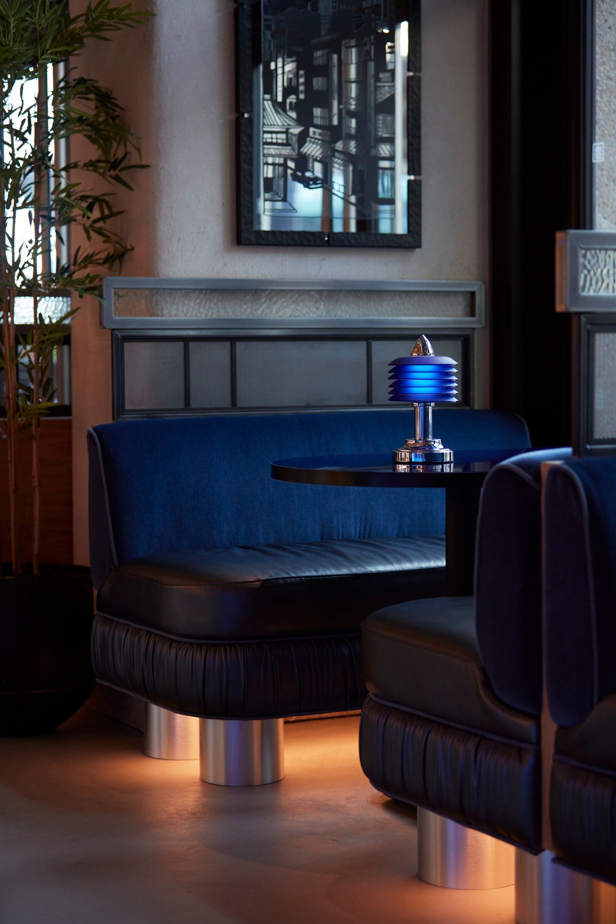 Midnight blue velvet booth seating with black table and illuminated blue cylindrical lamp in Wolves of Tokyo restaurant interior
