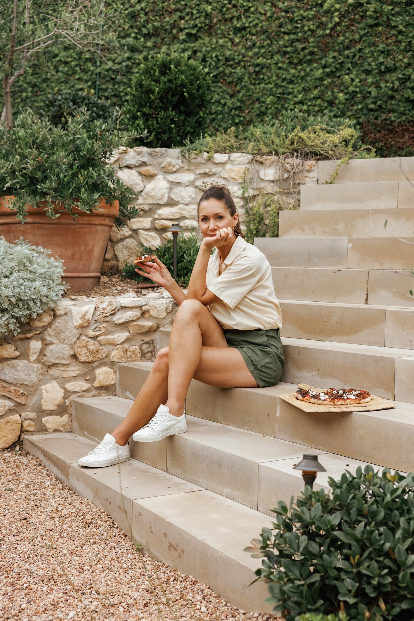 A guest holding a pizza while seated on garden steps