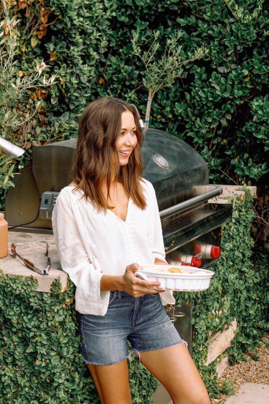 Home cook holding a baking dish beside a backyard grill