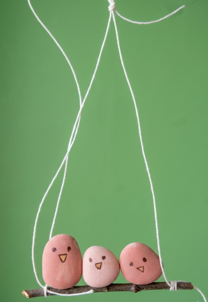 A finished hanging made from three painted pebble sparrows perched on a twig