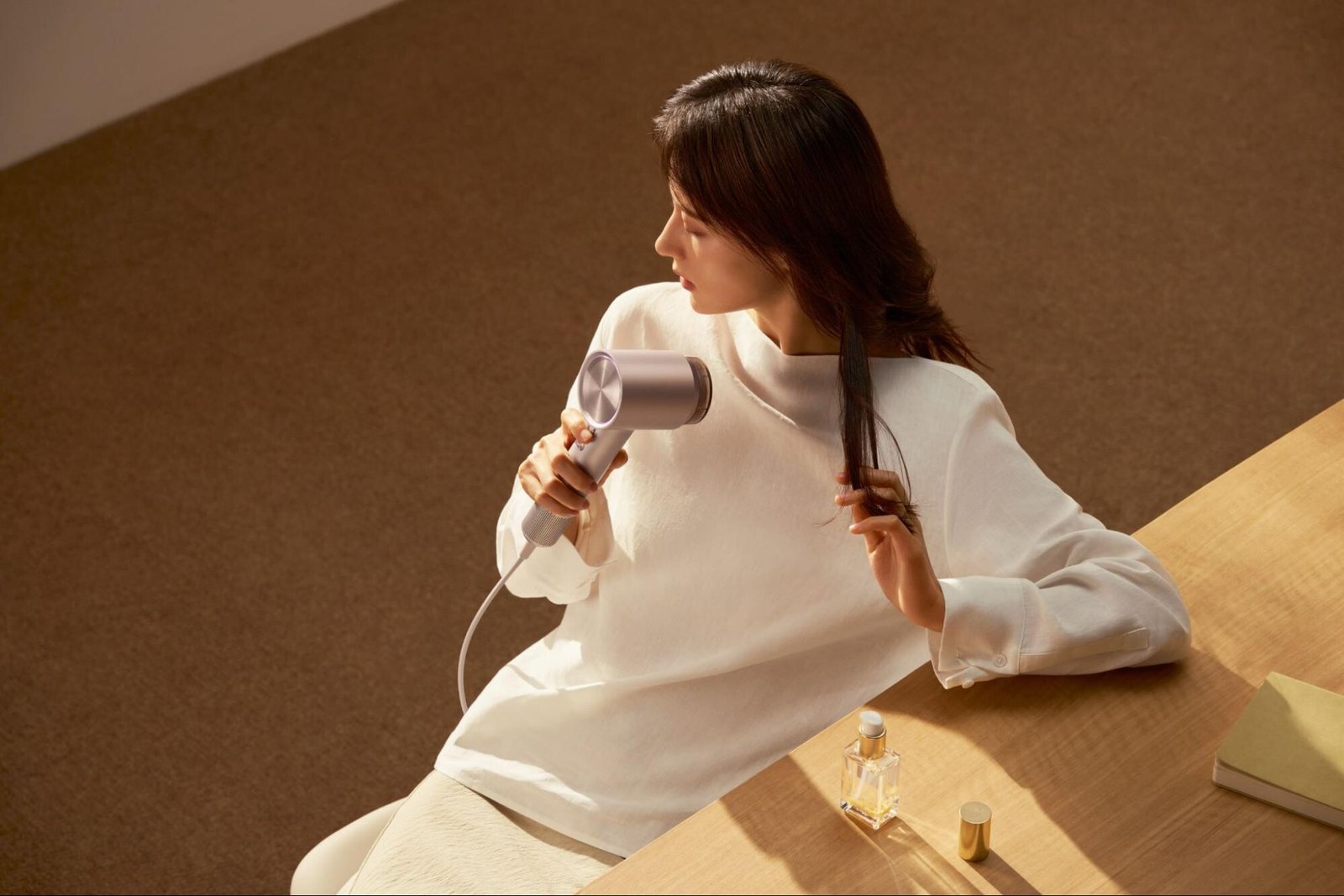 A woman using the Laifen Swift 4 hair dryer beside a bottle of hair oil