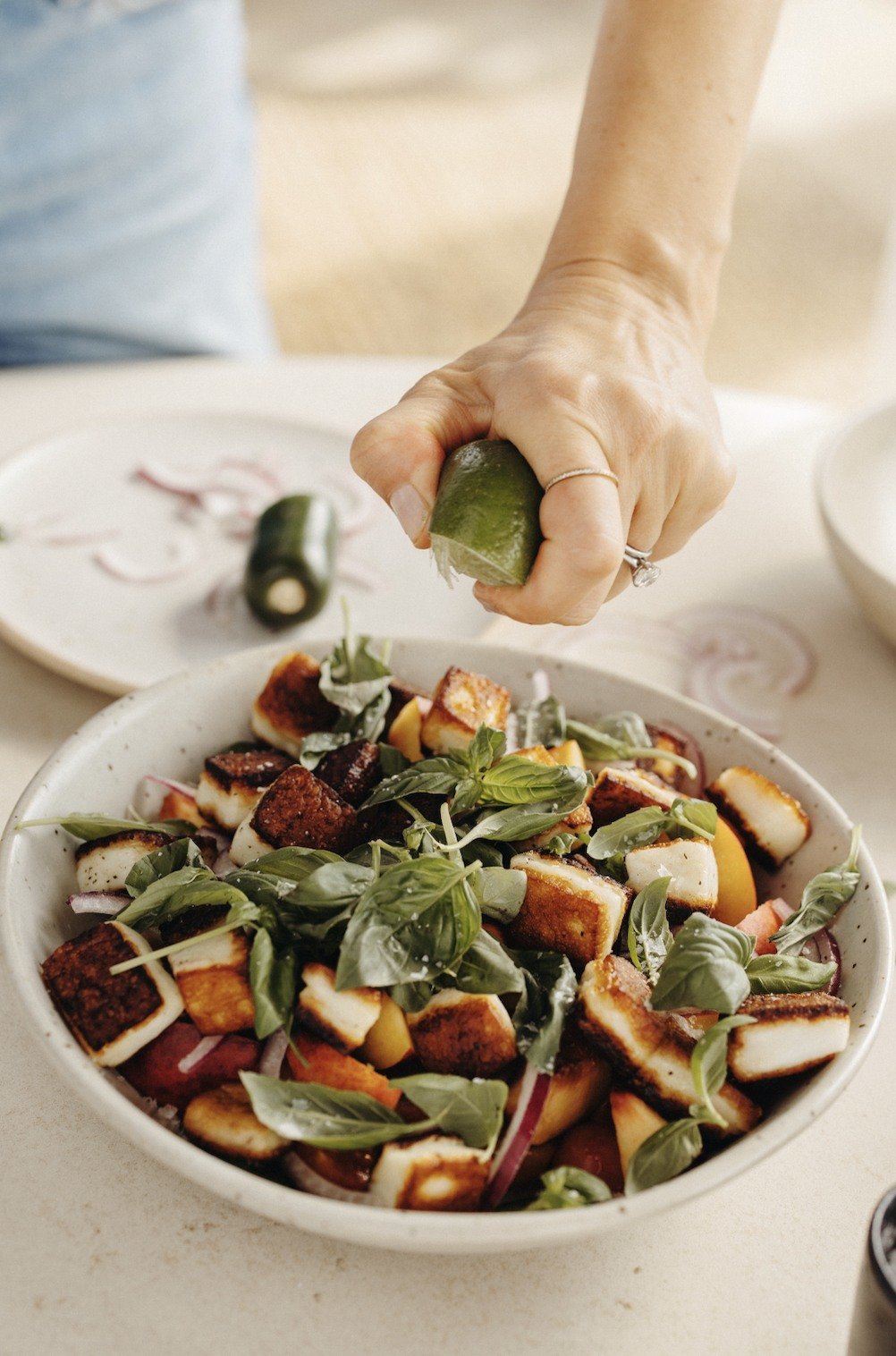 A hand squeezing lime over tomato, nectarine, and halloumi salad