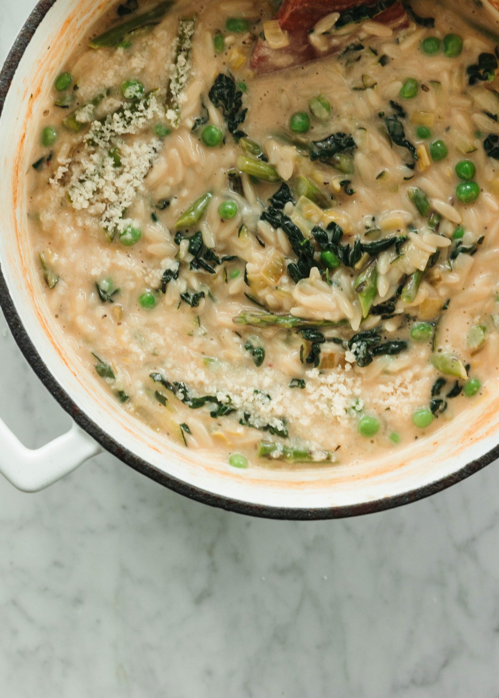 Creamy spring orzo with peas and kale in a white cooking pot