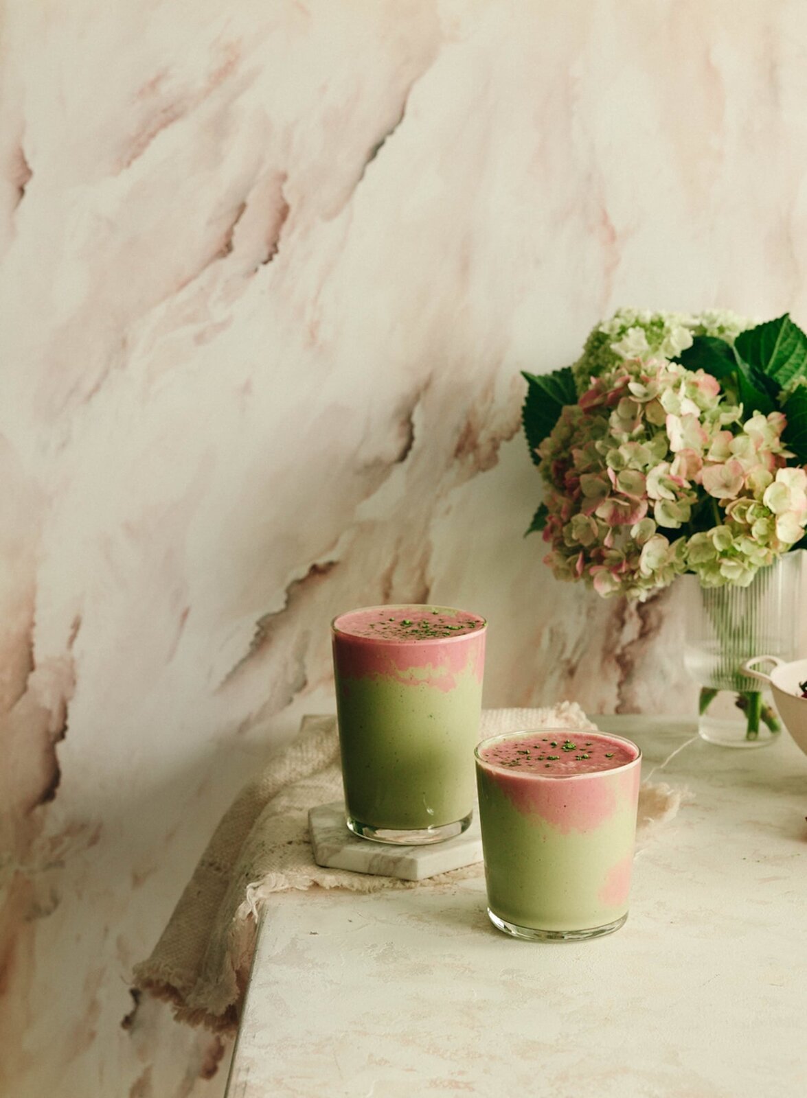 Two strawberry matcha smoothies on a pale stone table