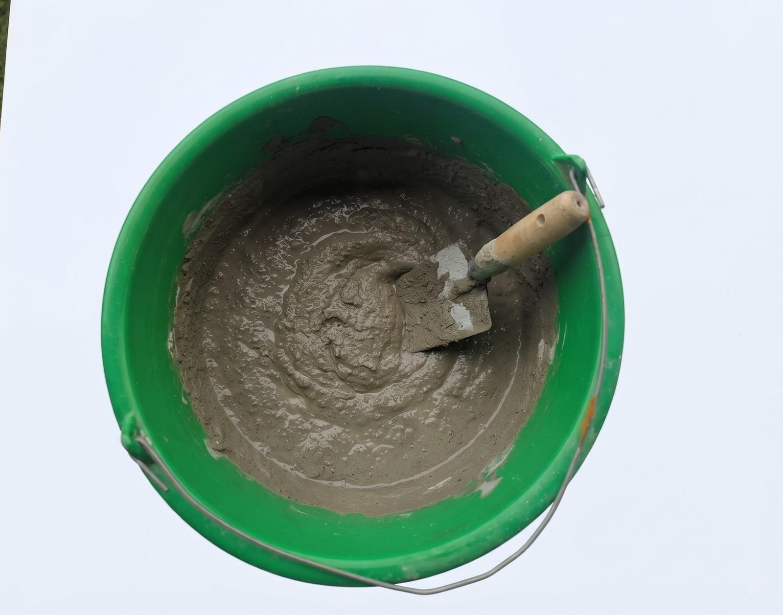 Wet cement mixed to a thick paste in a green bucket with a hand trowel