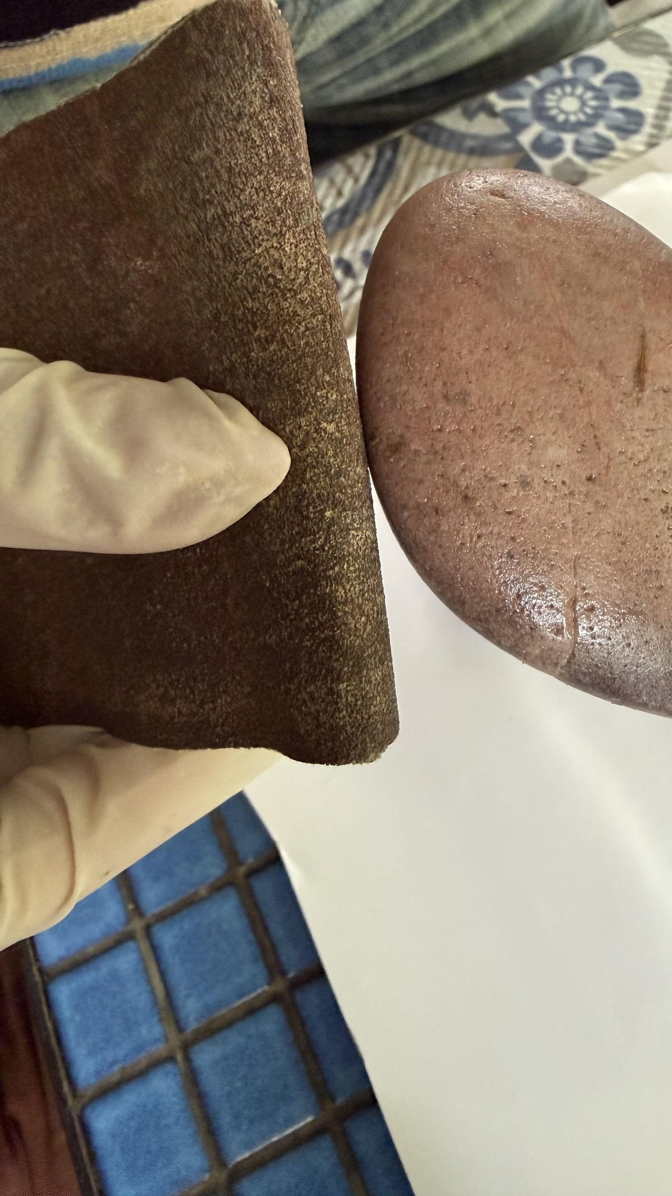 A gloved hand roughening a stone surface with sandpaper before gluing