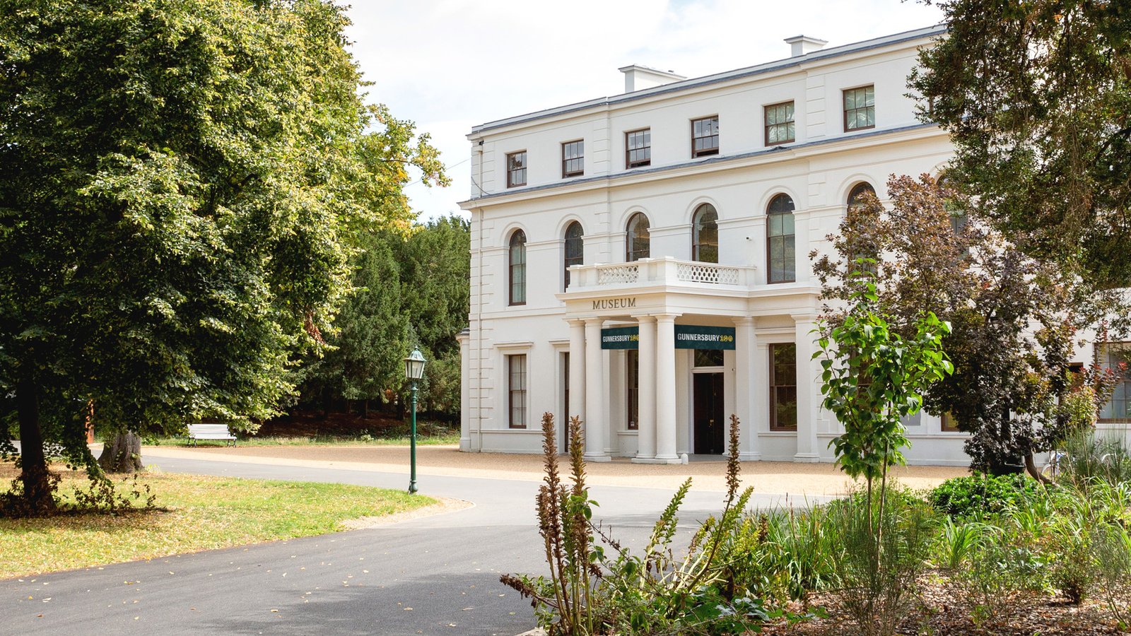 Cream-coloured neoclassical building with arched windows and columns, surrounded by mature trees and manicured grounds at Gunnersbury Park and Museum