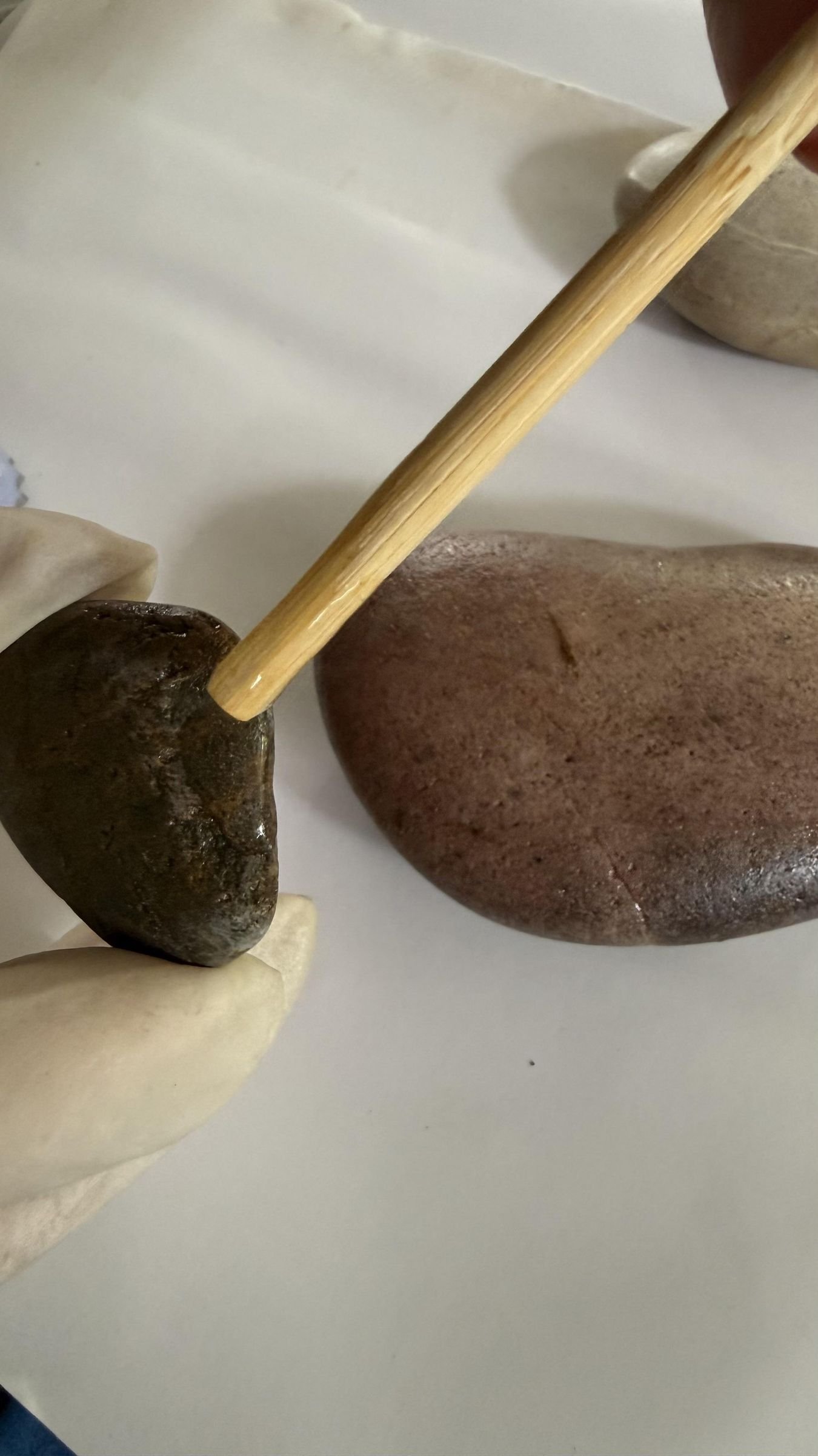 A wooden stick mixing two-part epoxy beside the stones to be joined