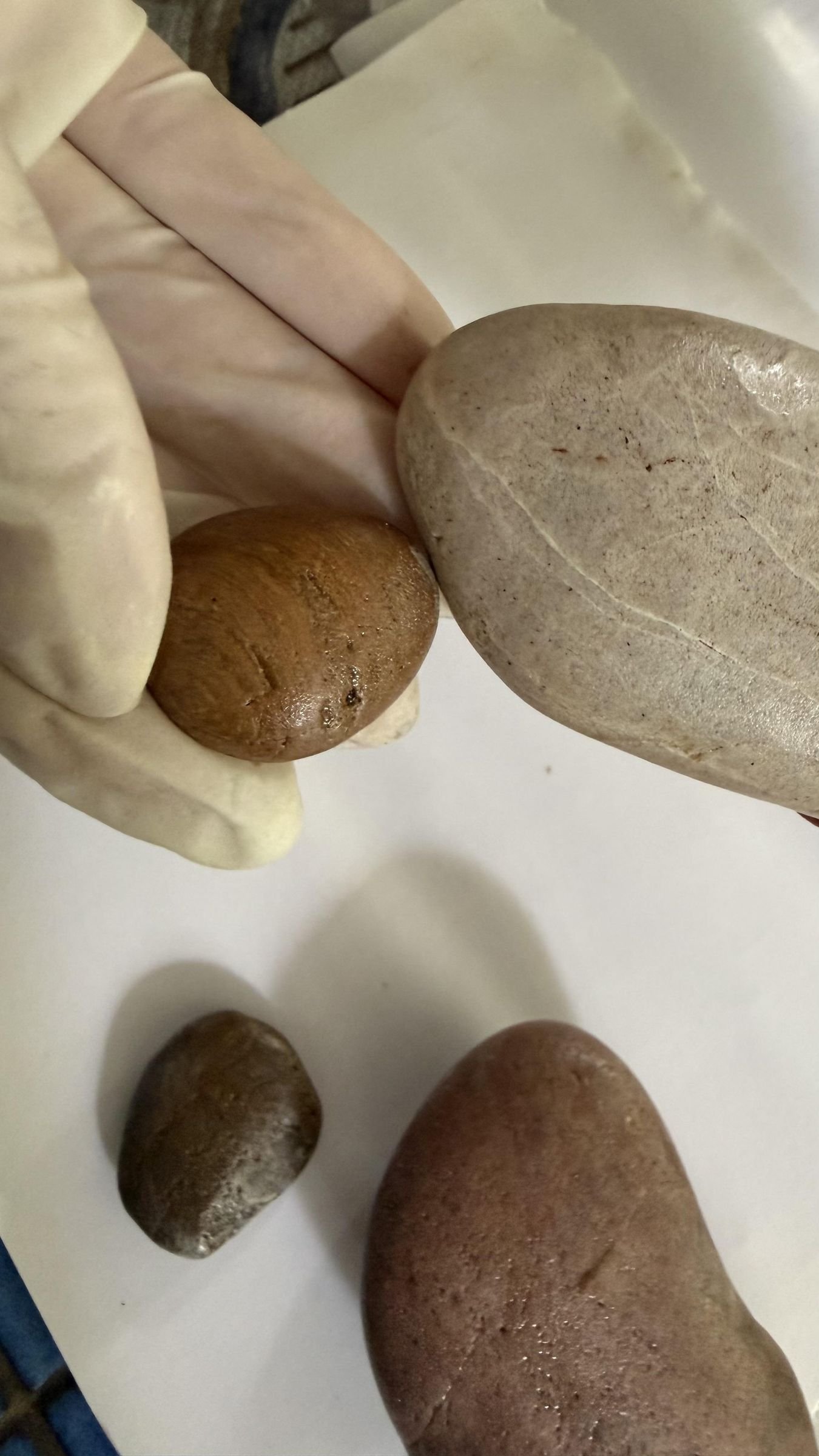 A gloved hand positioning a small stone against a larger stone with epoxy