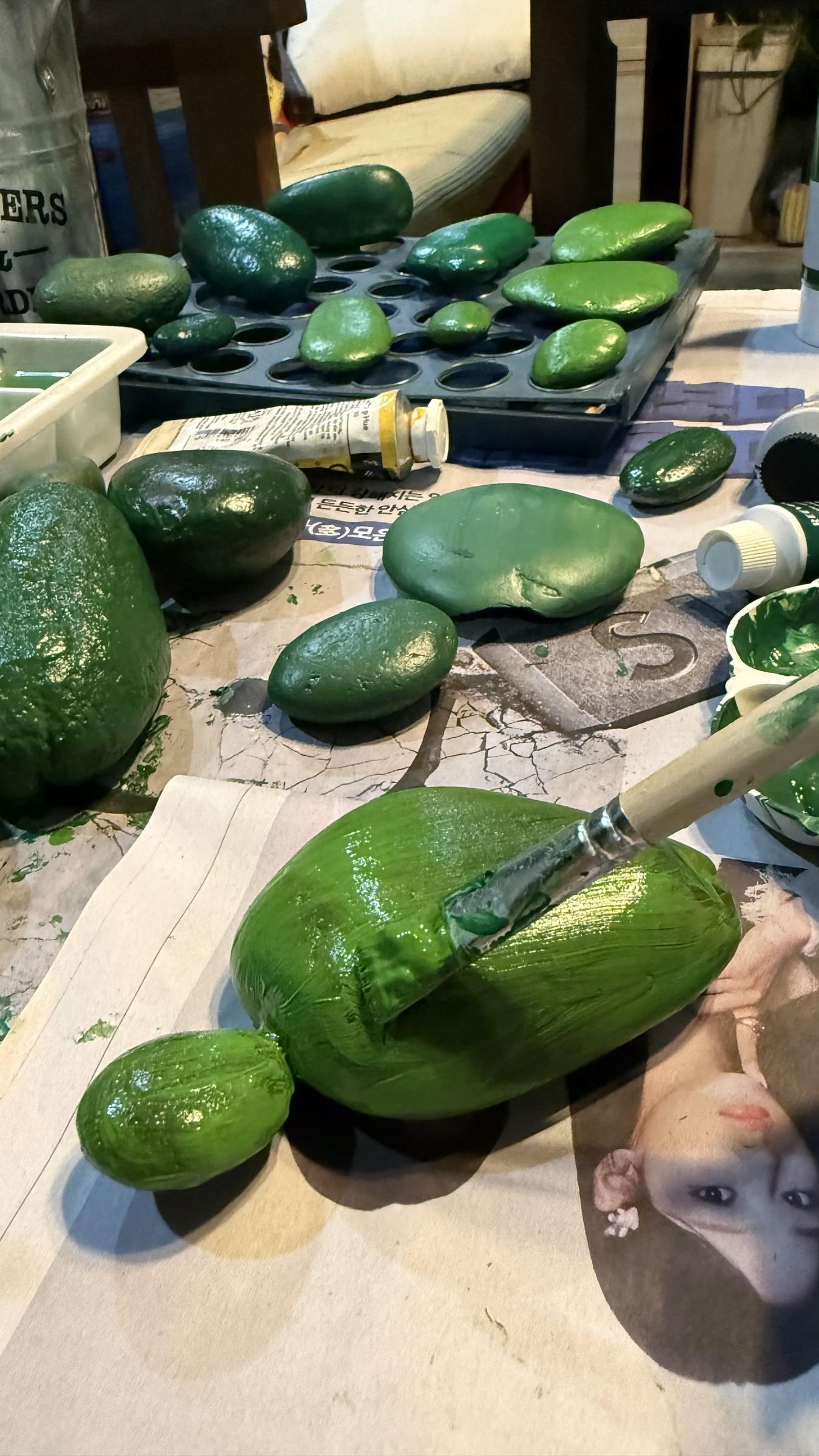 Several stone cactus shapes receiving green acrylic paint at the craft table
