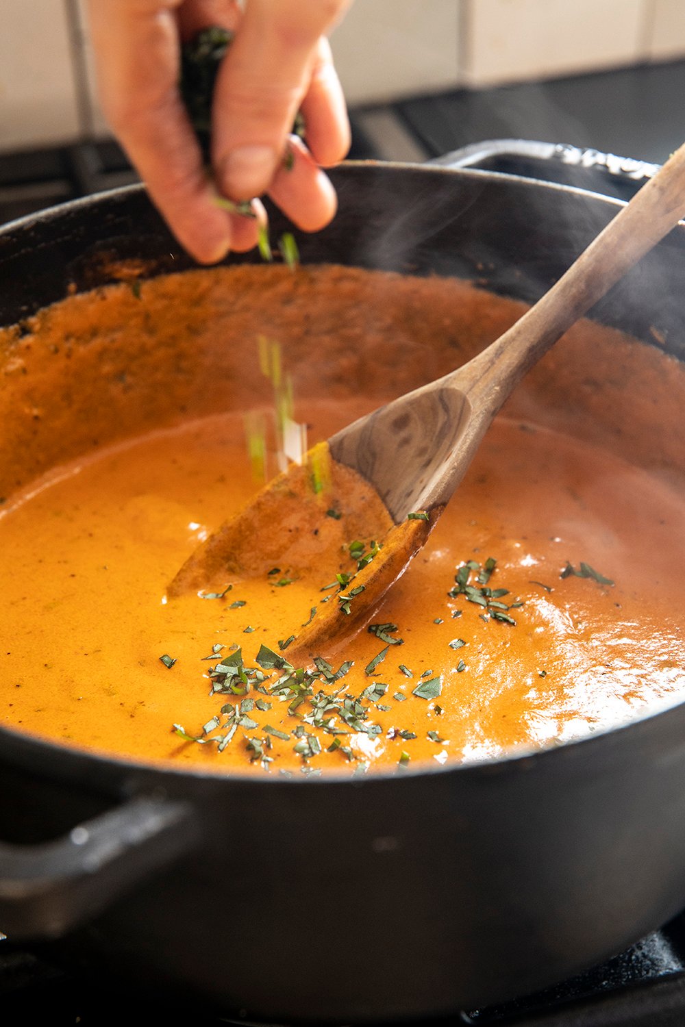 Basil being sprinkled into creamy tomato-vodka sauce in a skillet