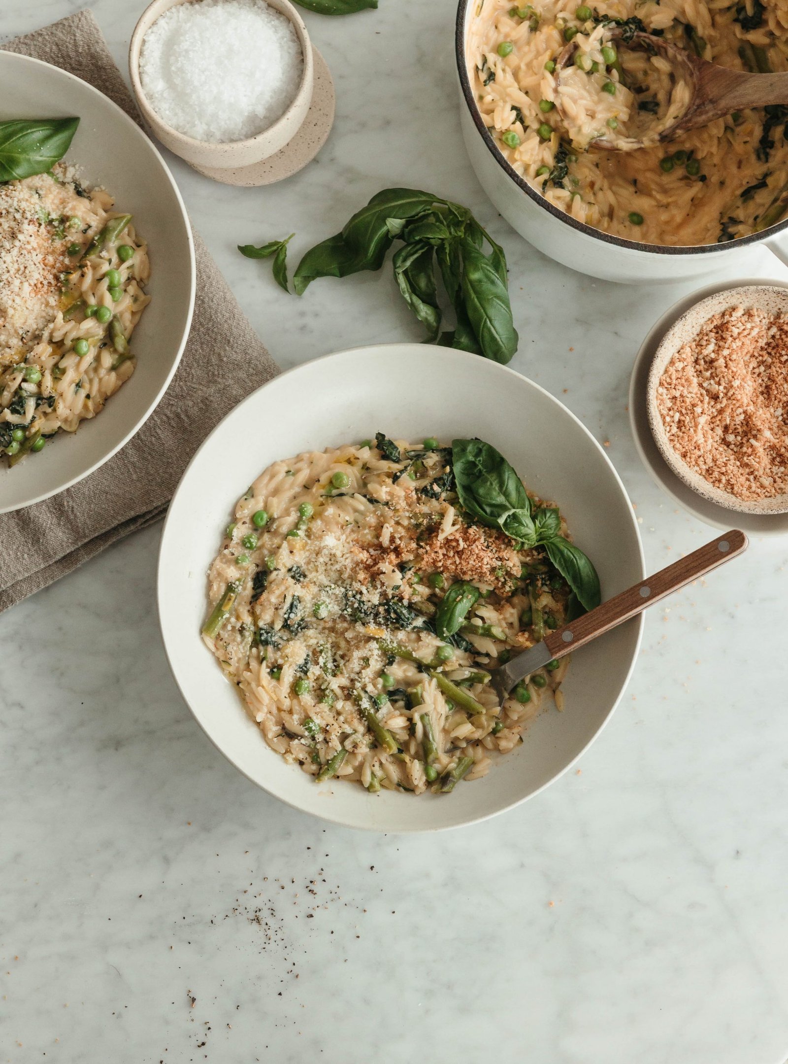 Bowls and a pot of creamy spring orzo on a marble table