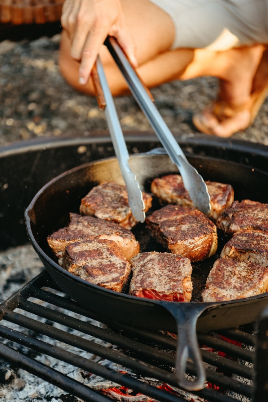 Steaks searing in a cast-iron skillet over a charcoal grill