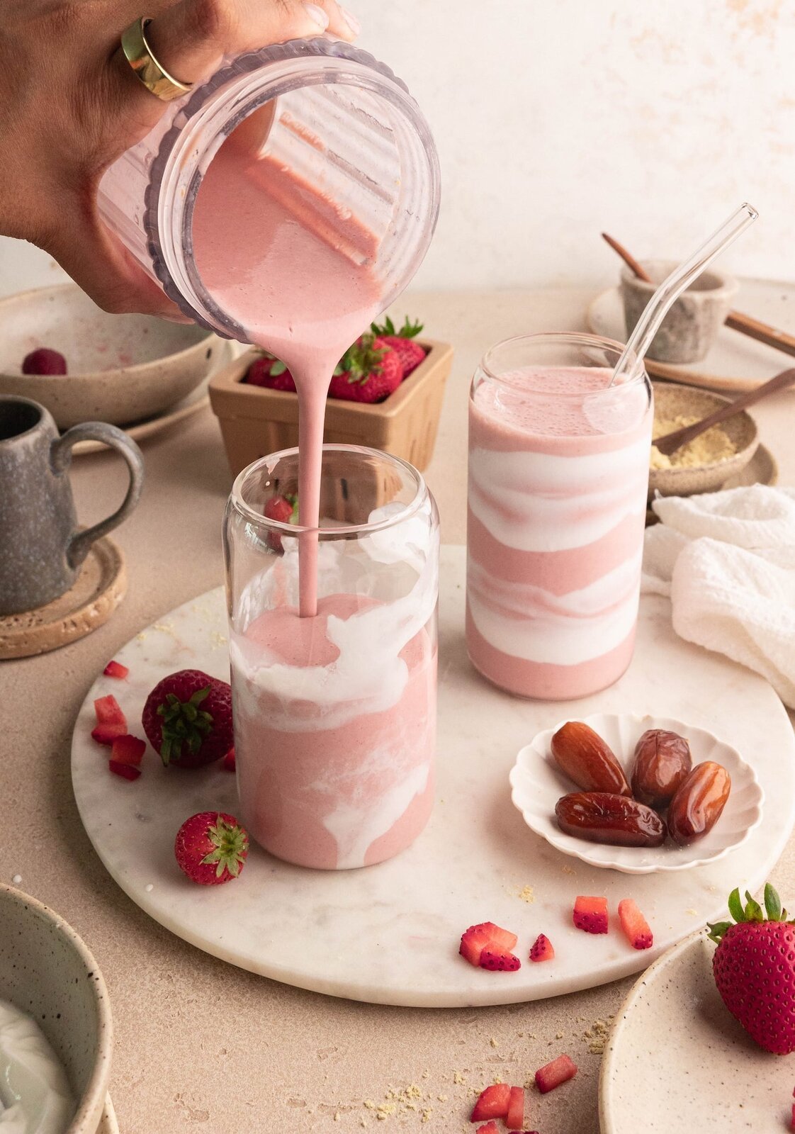 Pink strawberry probiotic smoothie being poured into layered glasses