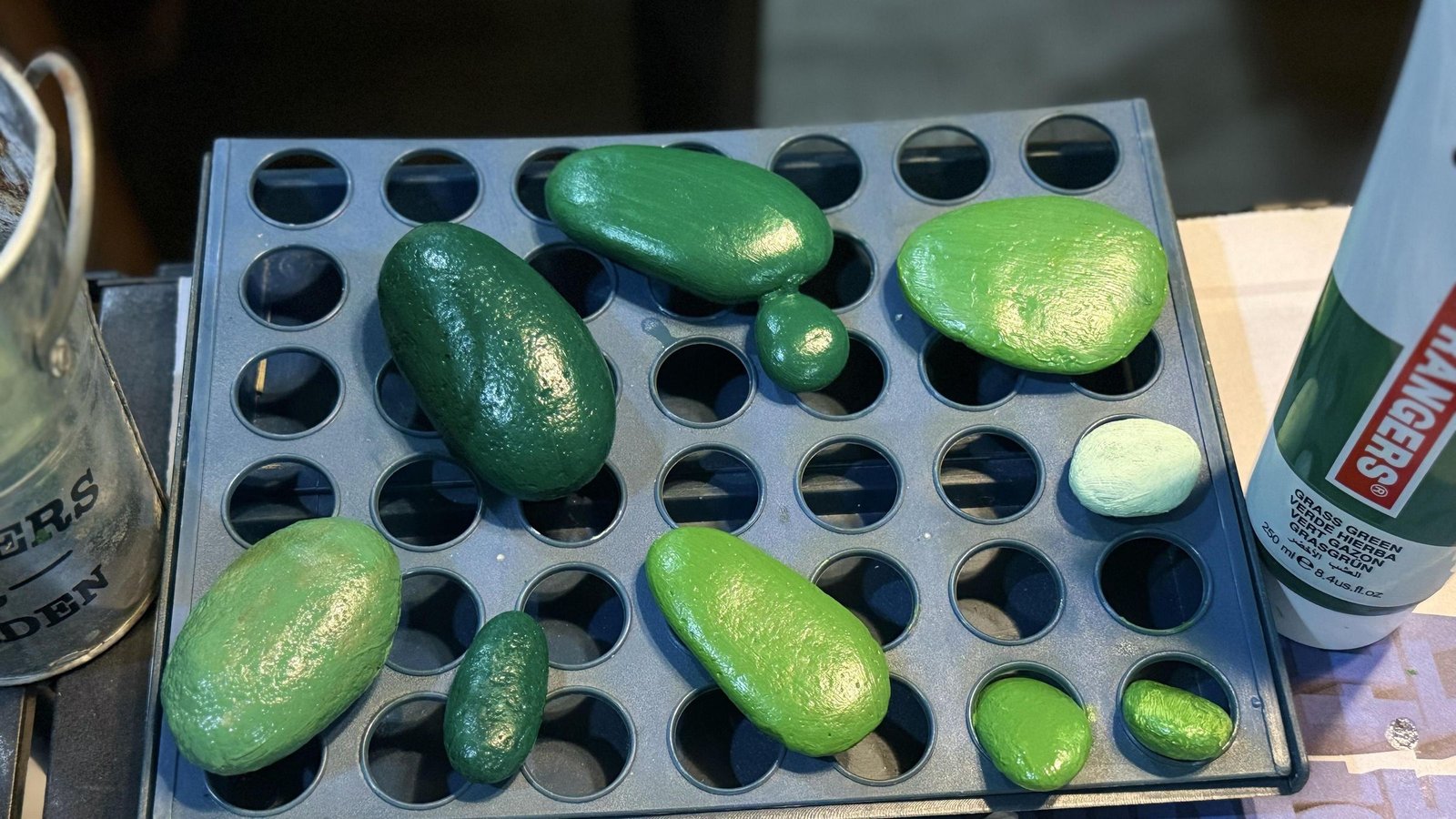 An assortment of green-painted stones drying on a black tray