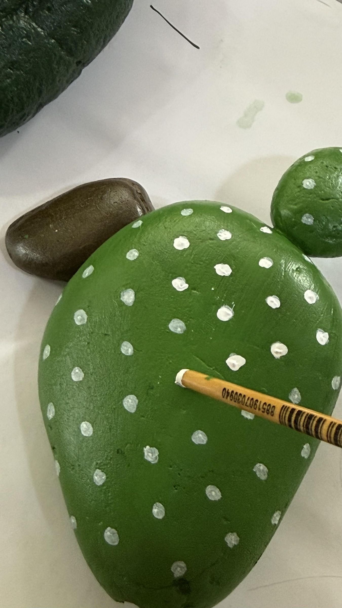 A small brush adding evenly spaced white dots to a rounded green cactus stone