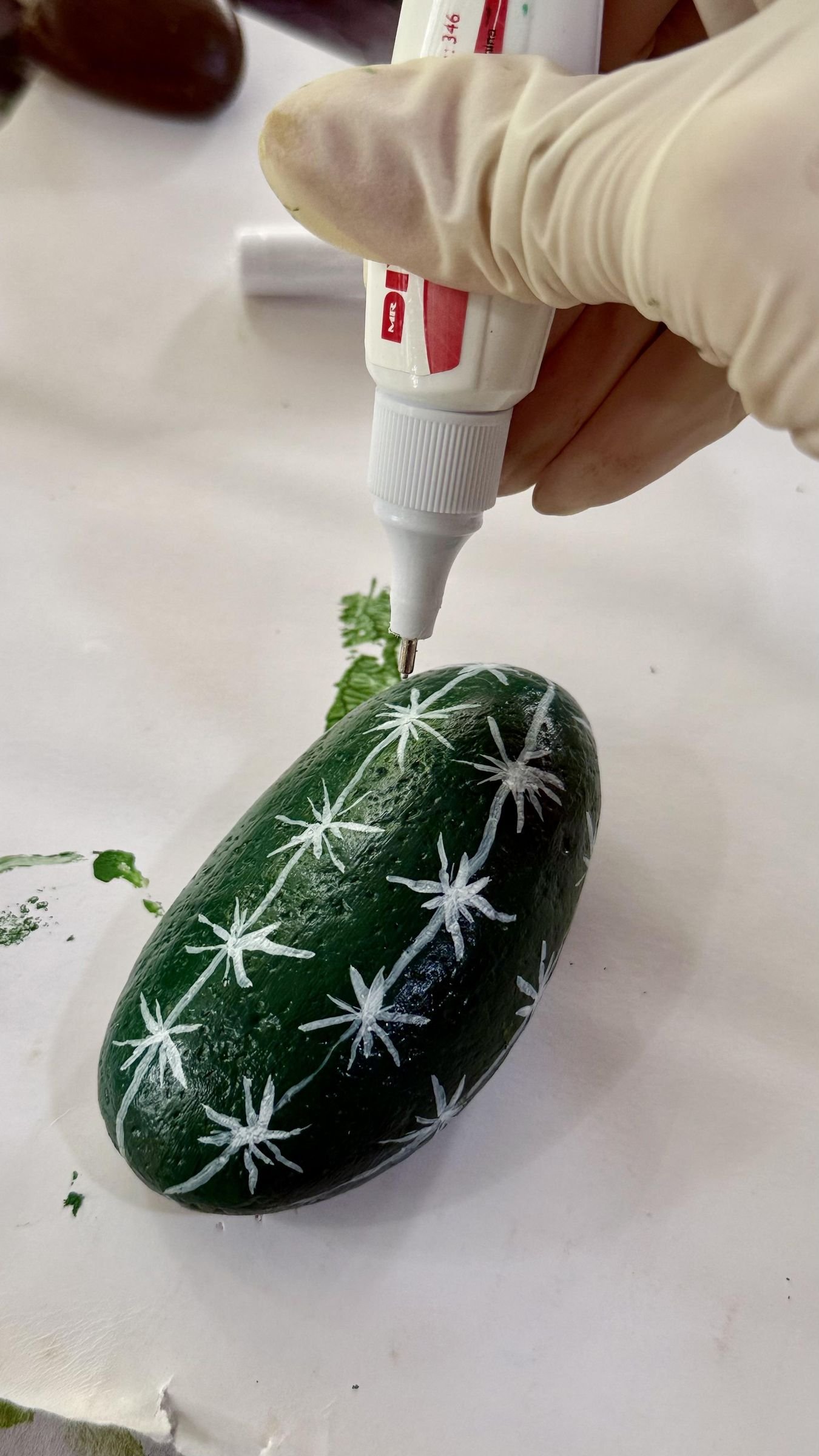 A white paint marker drawing starburst spine patterns on a dark green stone