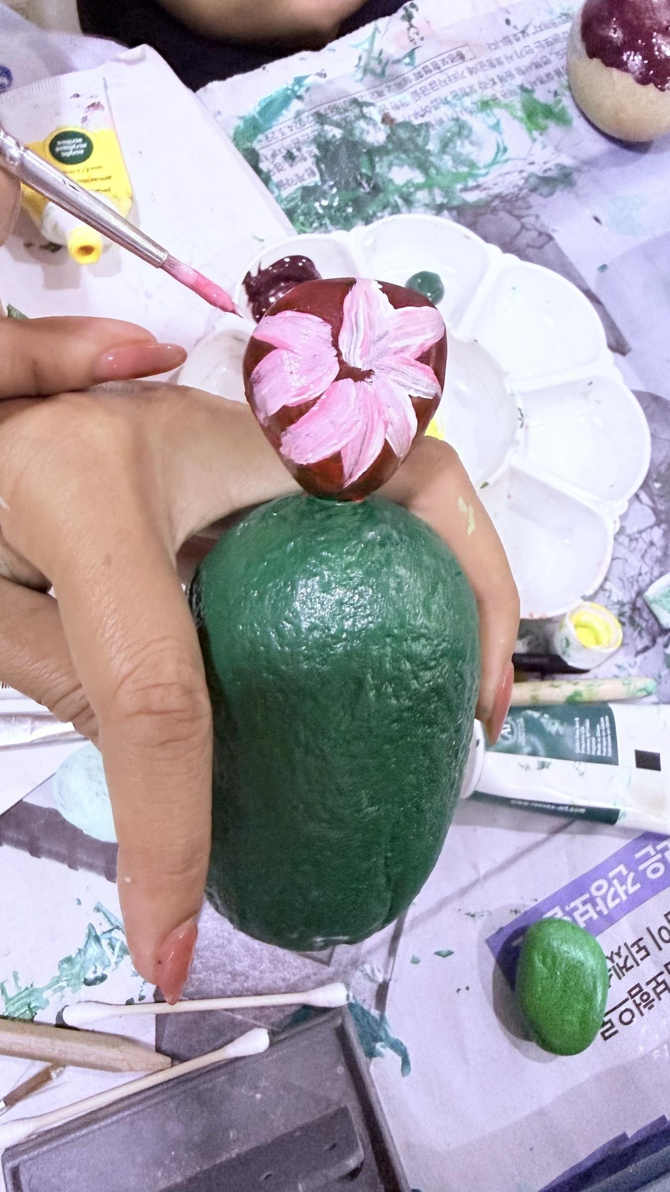A hand painting layered pink petals on a small stone attached to a cactus body