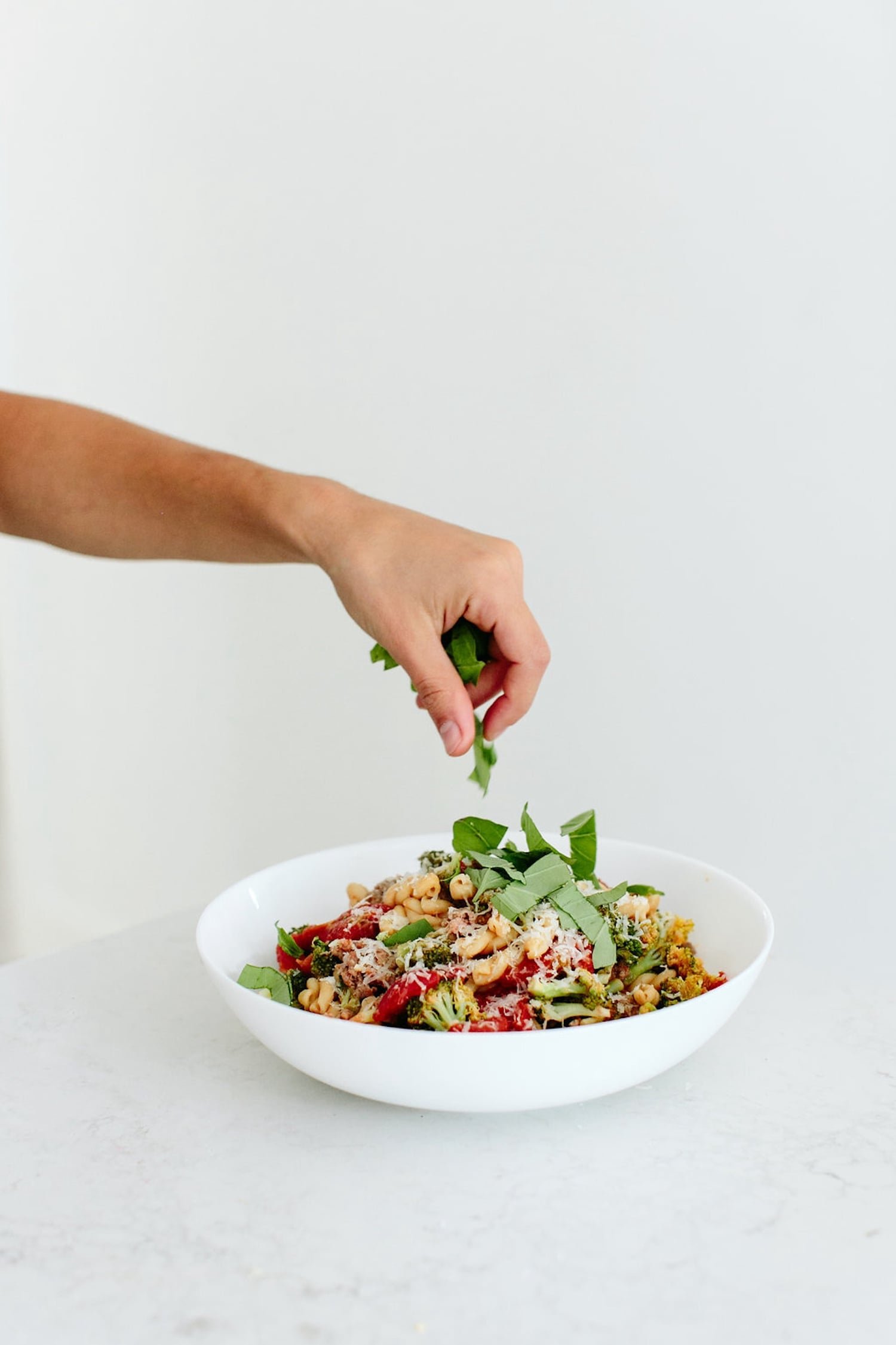 Fresh basil being scattered over turkey sausage and broccoli gemelli