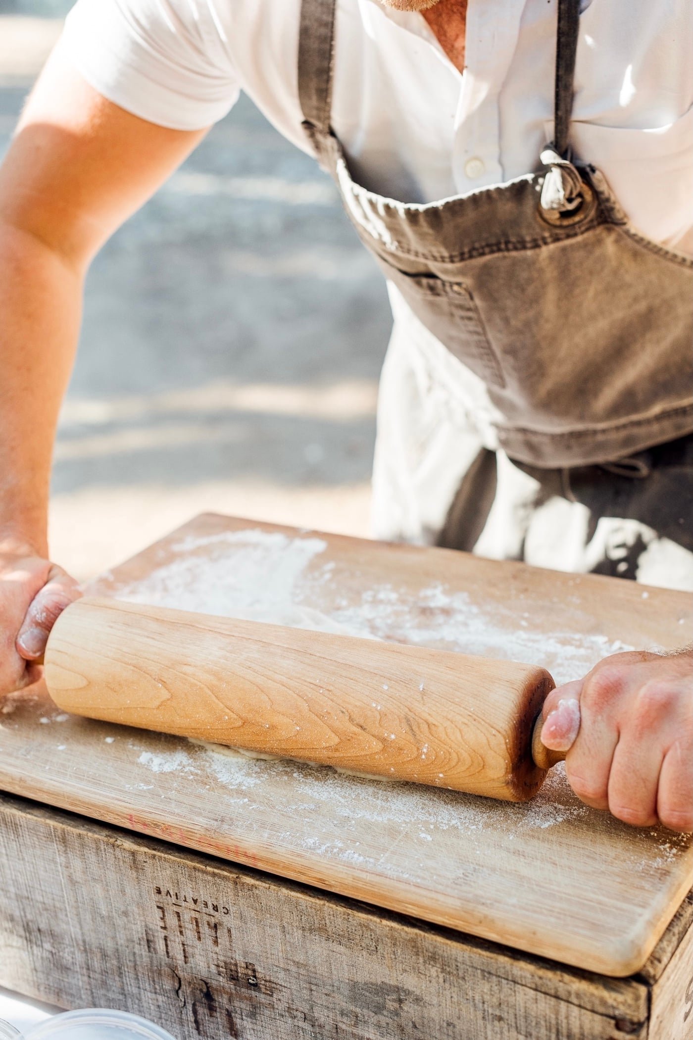 Hands rolling pizza dough on a floured wooden board