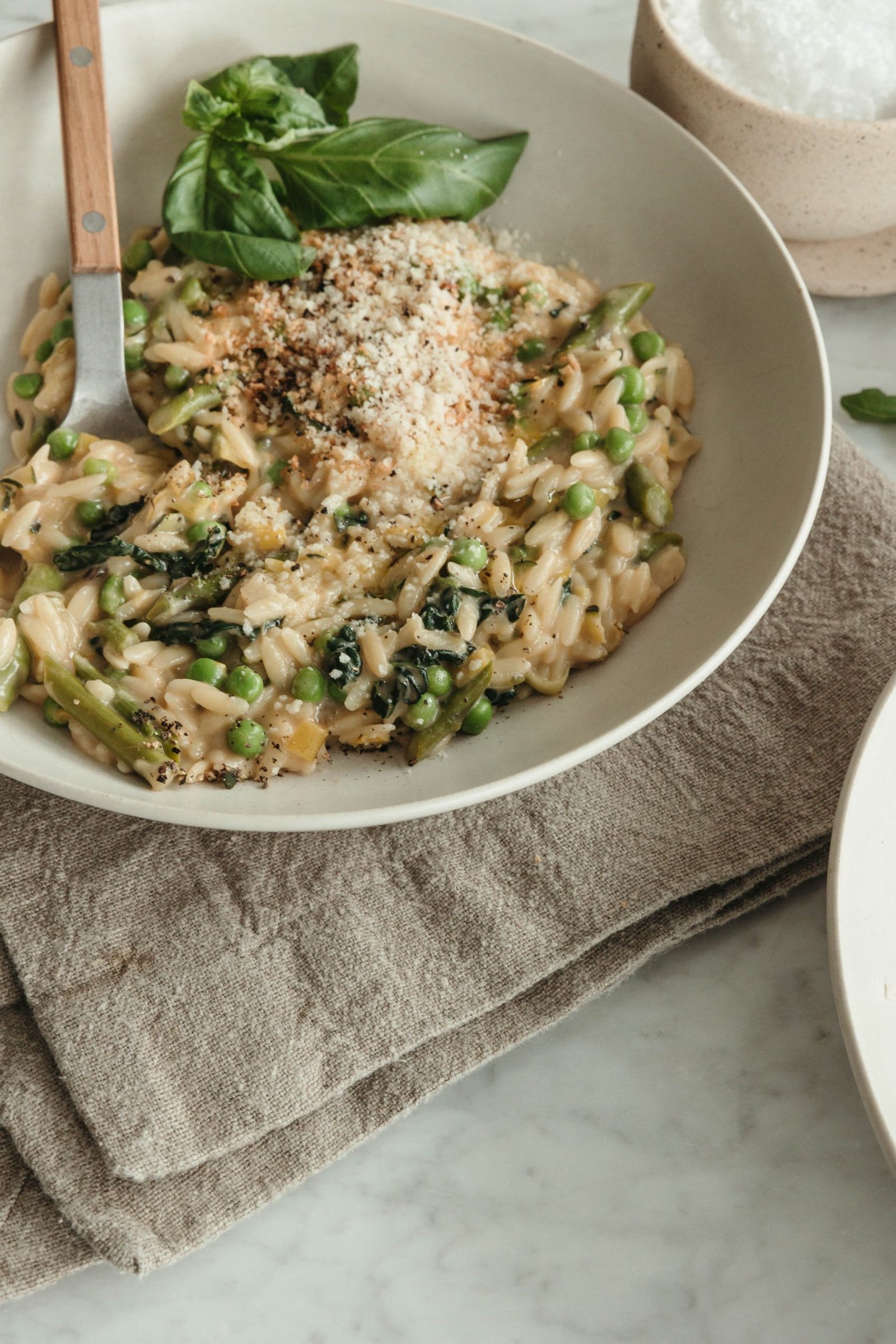 Creamy Parmesan orzo with peas and asparagus beside folded linen