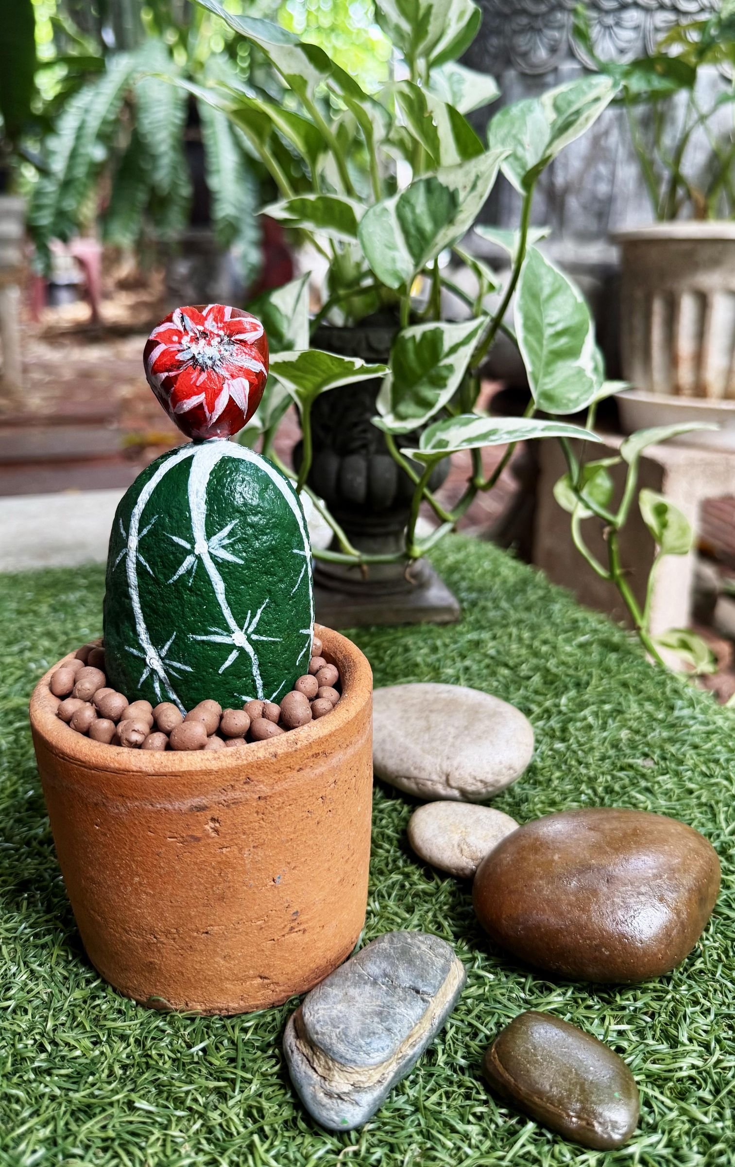 A single flowering stone cactus planter displayed beside loose smooth rocks