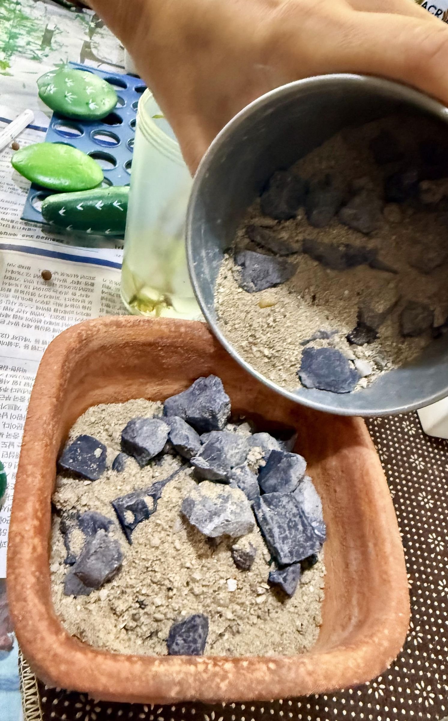 Sand and small stones being poured around cactus rocks in a terracotta planter