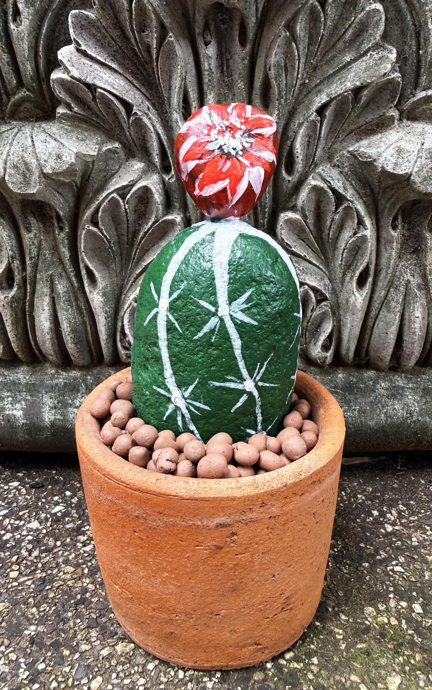 A finished single stone cactus with a red flower in a pebble-topped terracotta pot