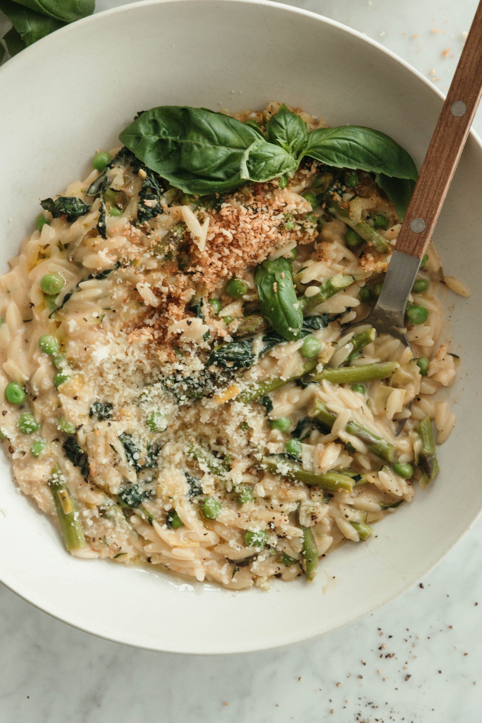 Close-up bowl of creamy orzo with Parmesan, peas, asparagus, and basil