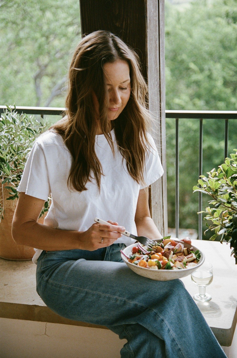 A woman enjoying tomato, nectarine, and halloumi salad by an open window