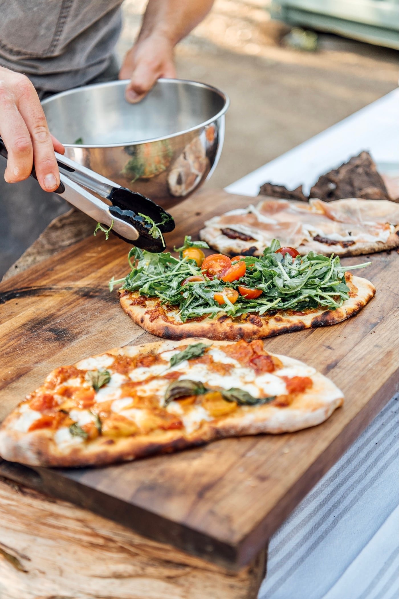 Olive oil being drizzled over arugula-topped pizzas