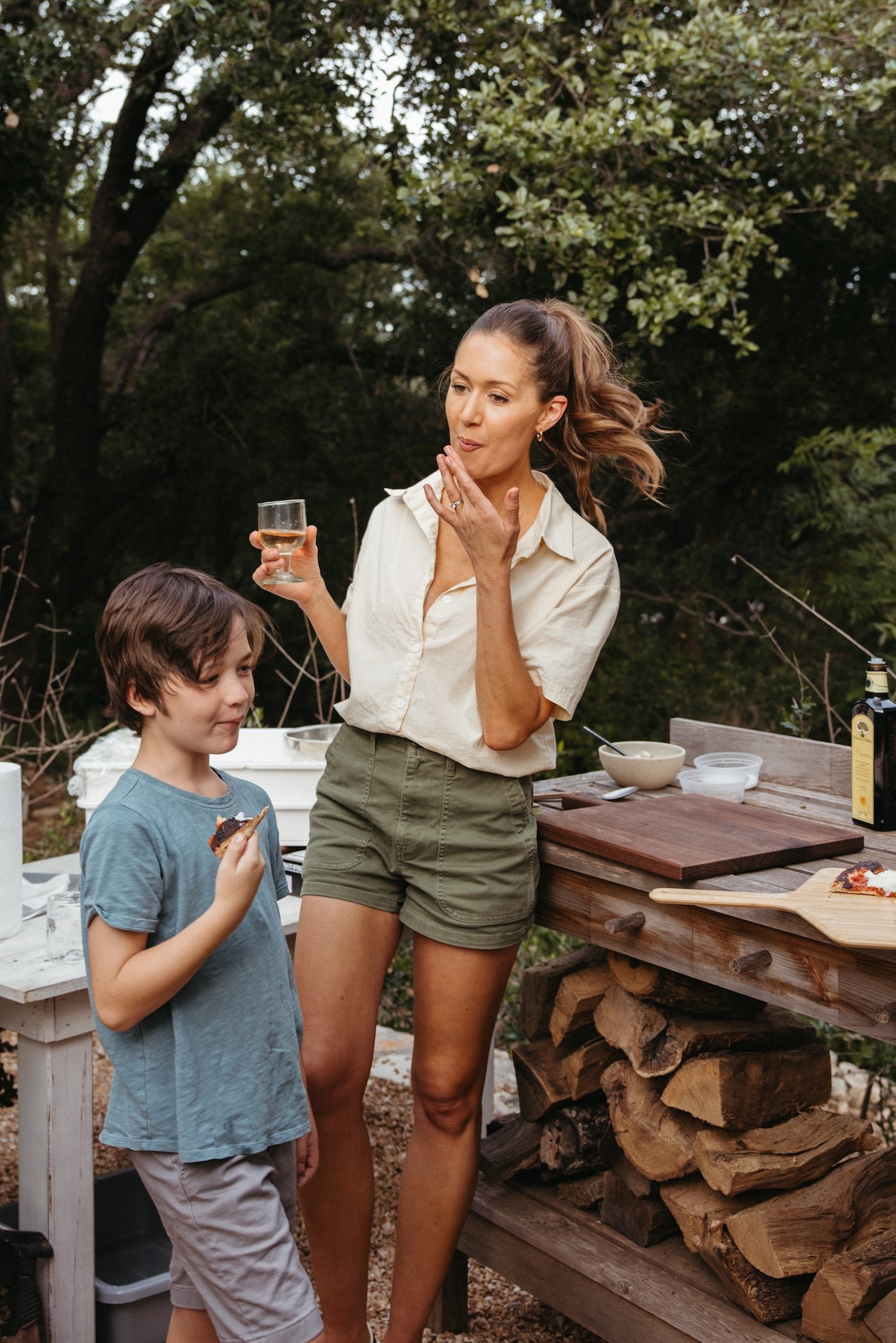 A woman and child tasting pizza beside an outdoor oven