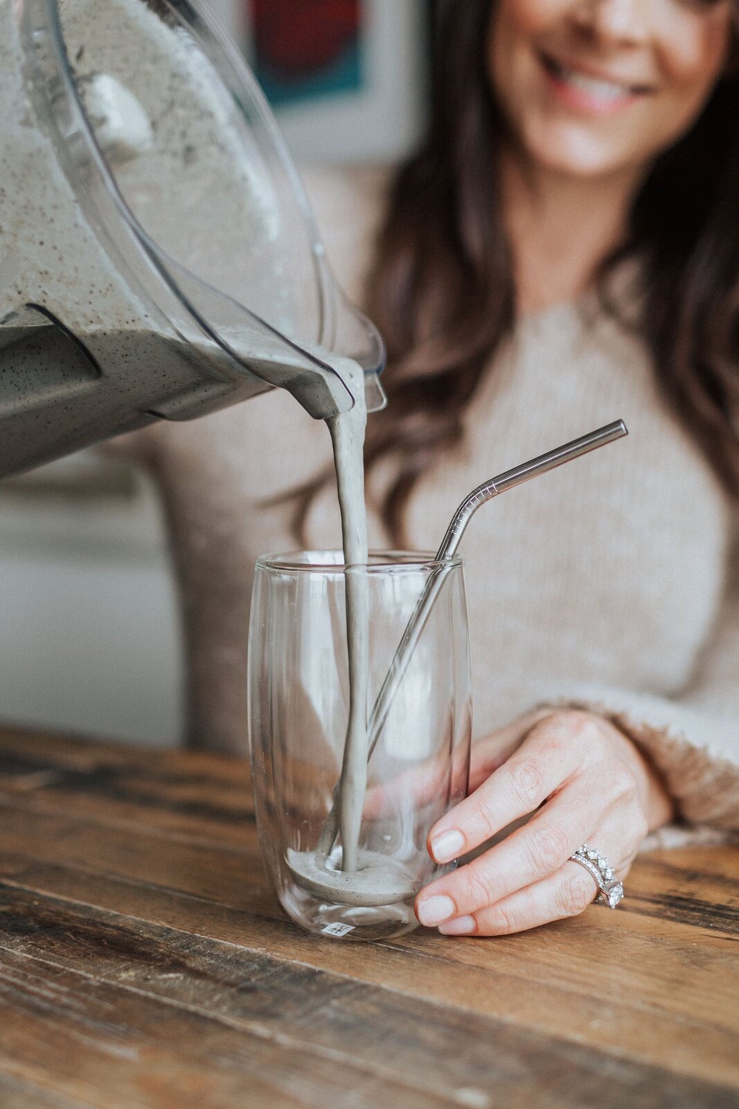 A woman pouring a chocolate protein smoothie into a clear glass