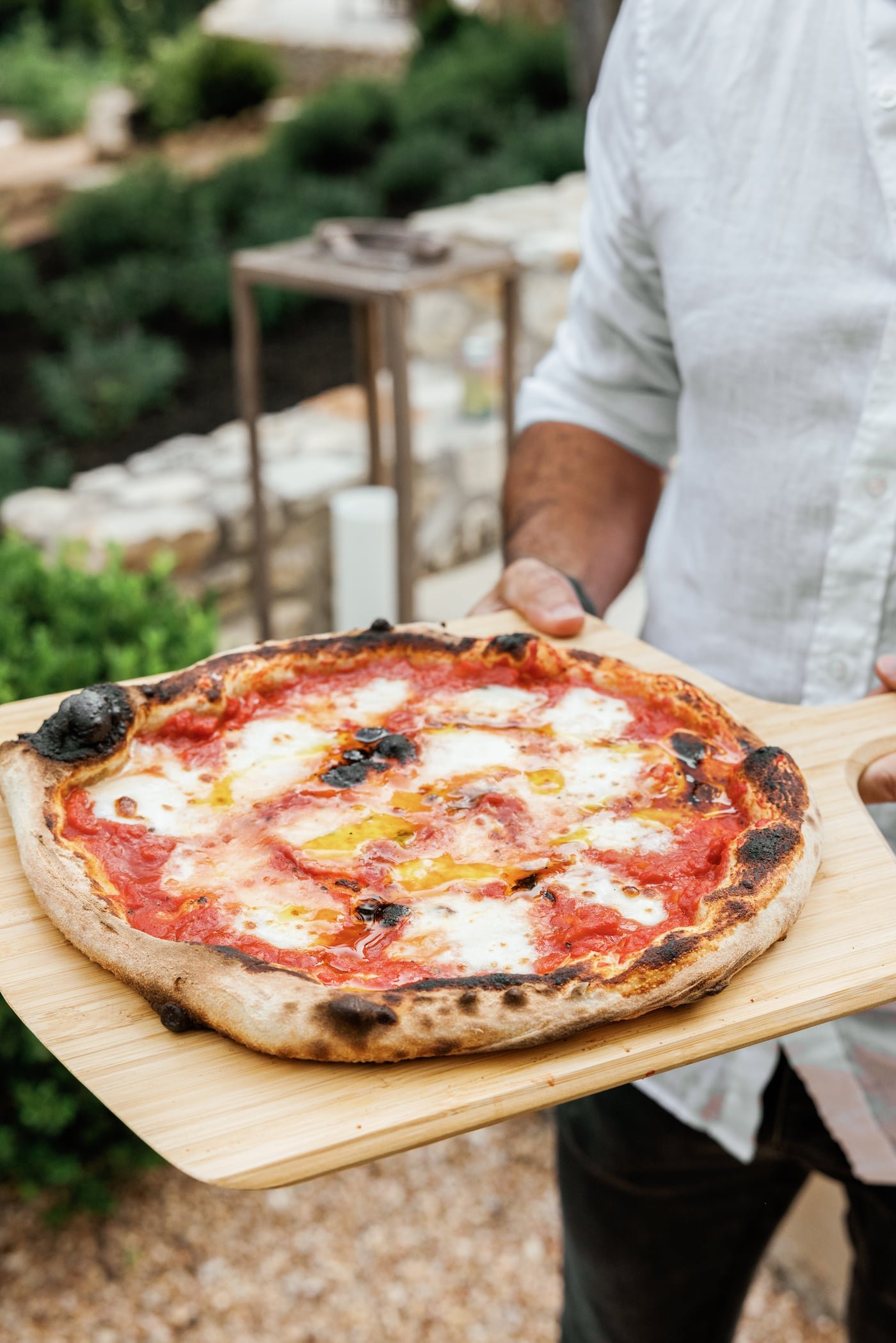 A finished tomato and burrata pizza resting on a wooden peel