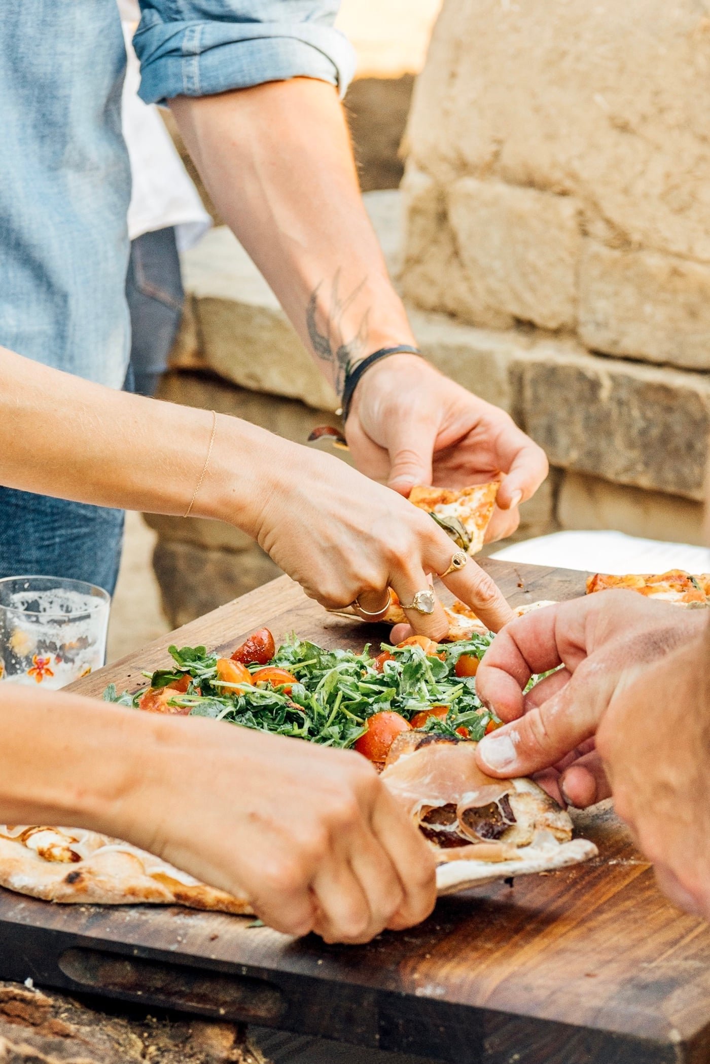Several hands slicing and sharing fresh pizza